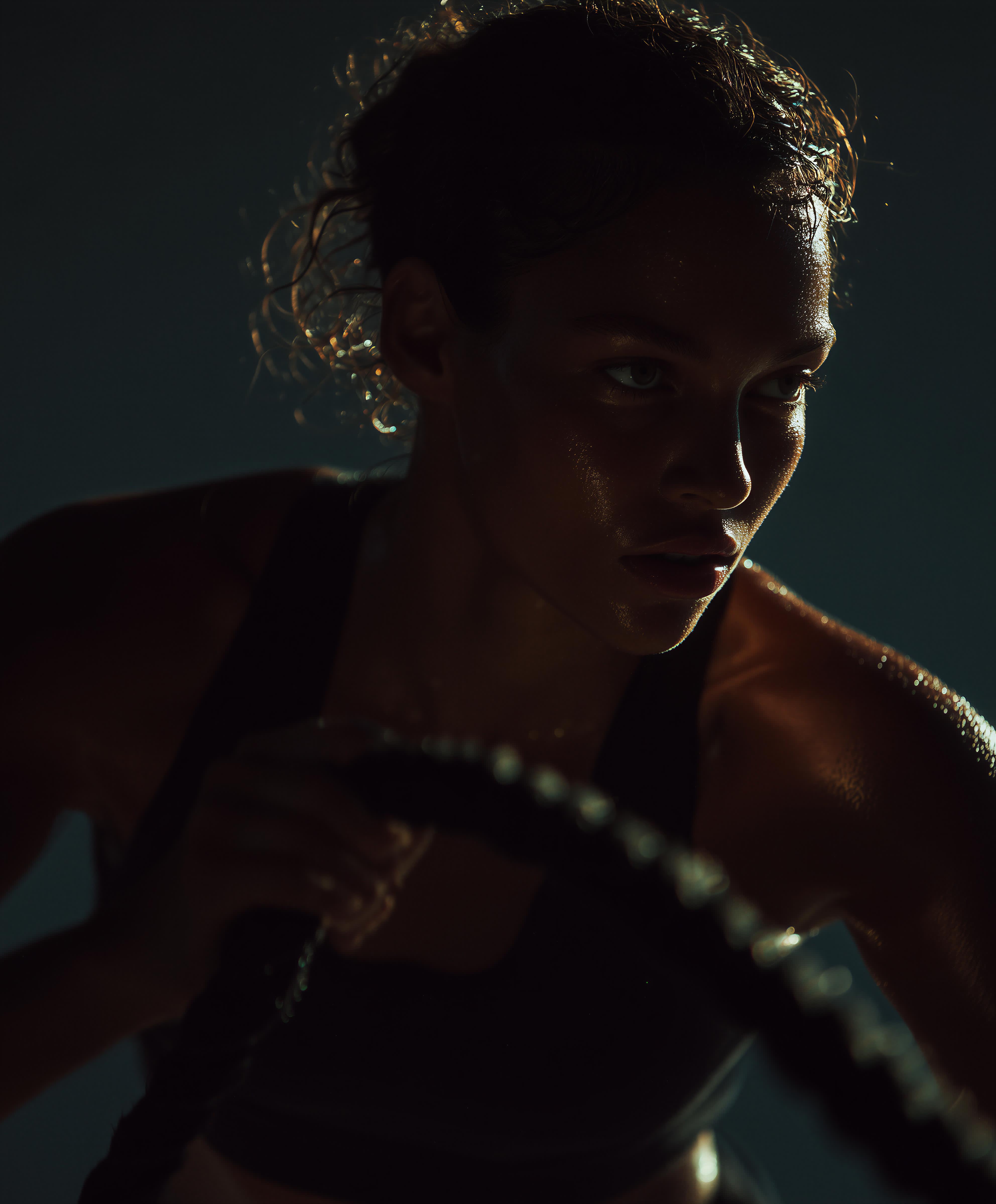 Close-up of a focused athlete exercising with battle ropes under dramatic low lighting, sweat glistening on her face.