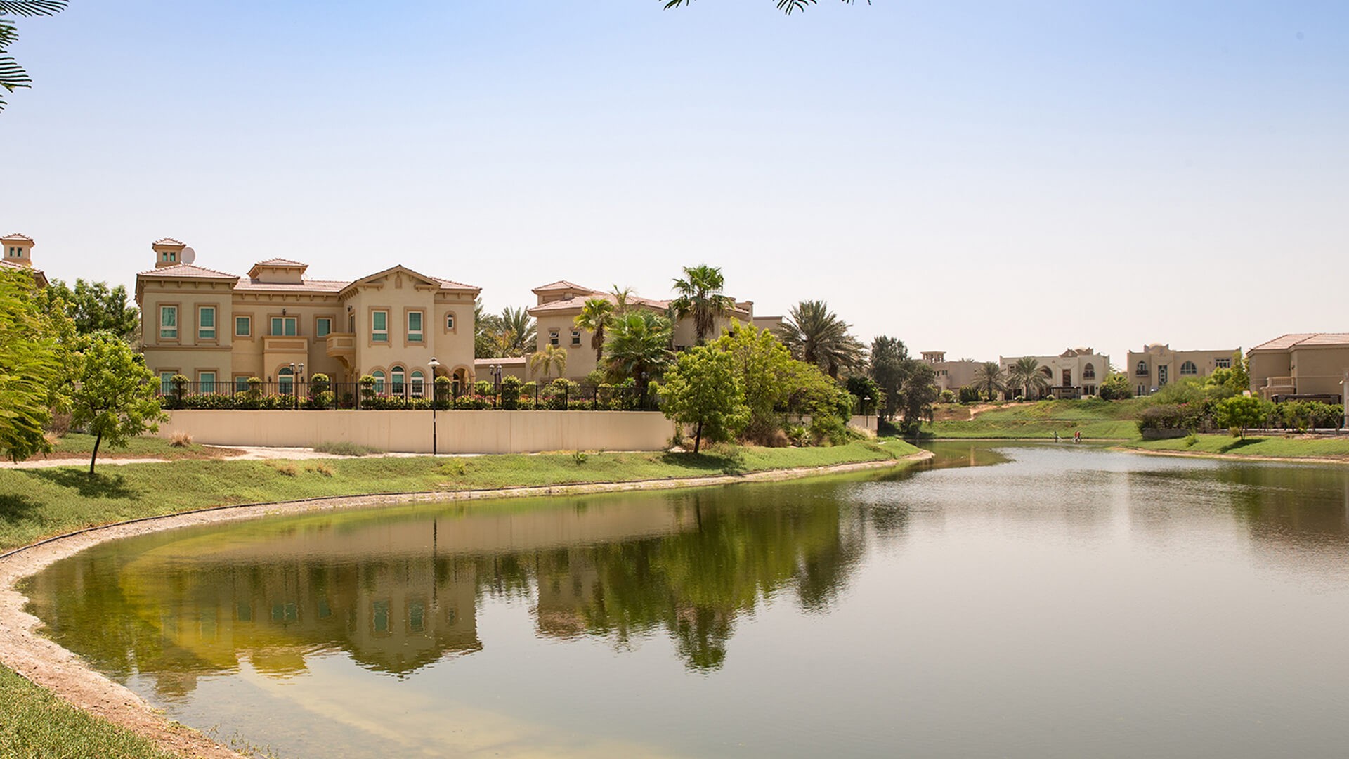A large house overlooks a calm lake and pond, surrounded by the scenic beauty of Jumeirah Islands.