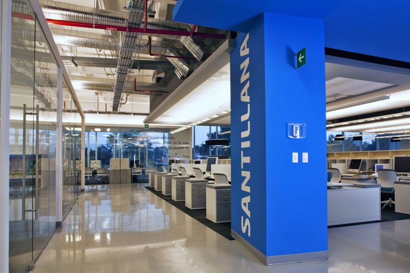 Female lab technician in protective gear using a high-tech analyzer while referencing data on dual computer screens in a laboratory setting.