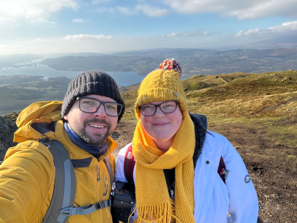 A selfie of Martin and April with Windermere in the background. Both dressed in winter clothes with wooly hats and scarfs.