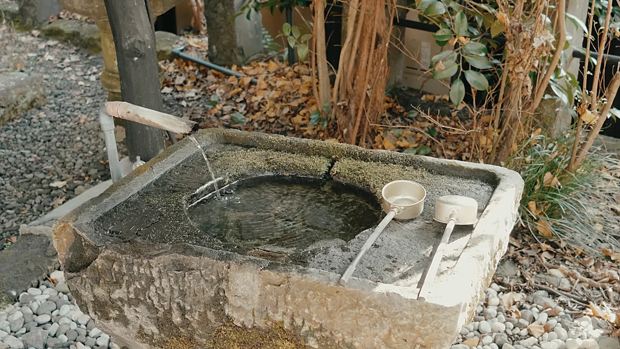 A stone water basin at Kurokawa Onsen with a bamboo spout and two wooden dippers