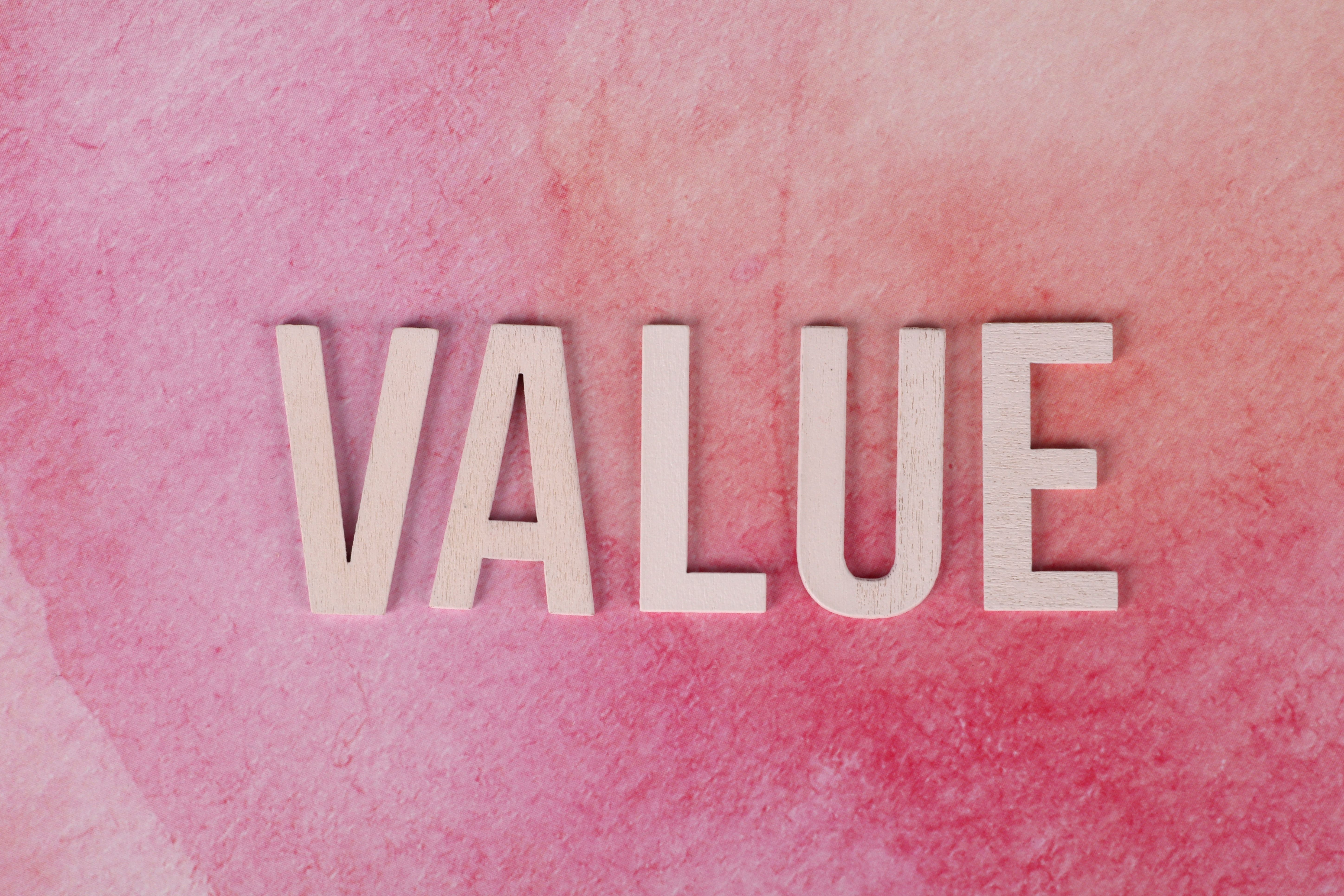 The word 'VALUE' spelled out in wooden letters on a pink watercolour background.