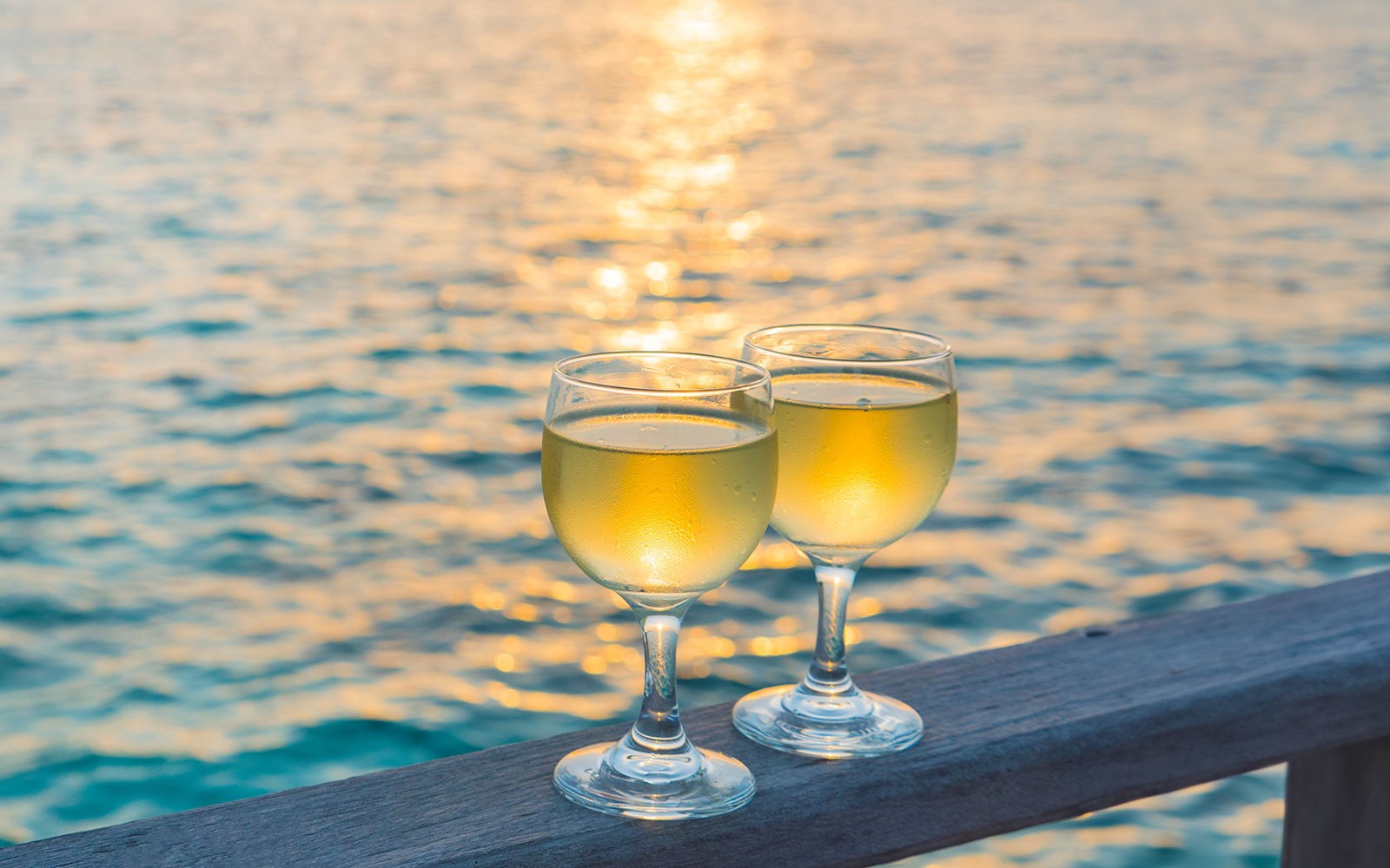 Two wine glasses on a railing with a sunset over the sea in Split, Croatia.