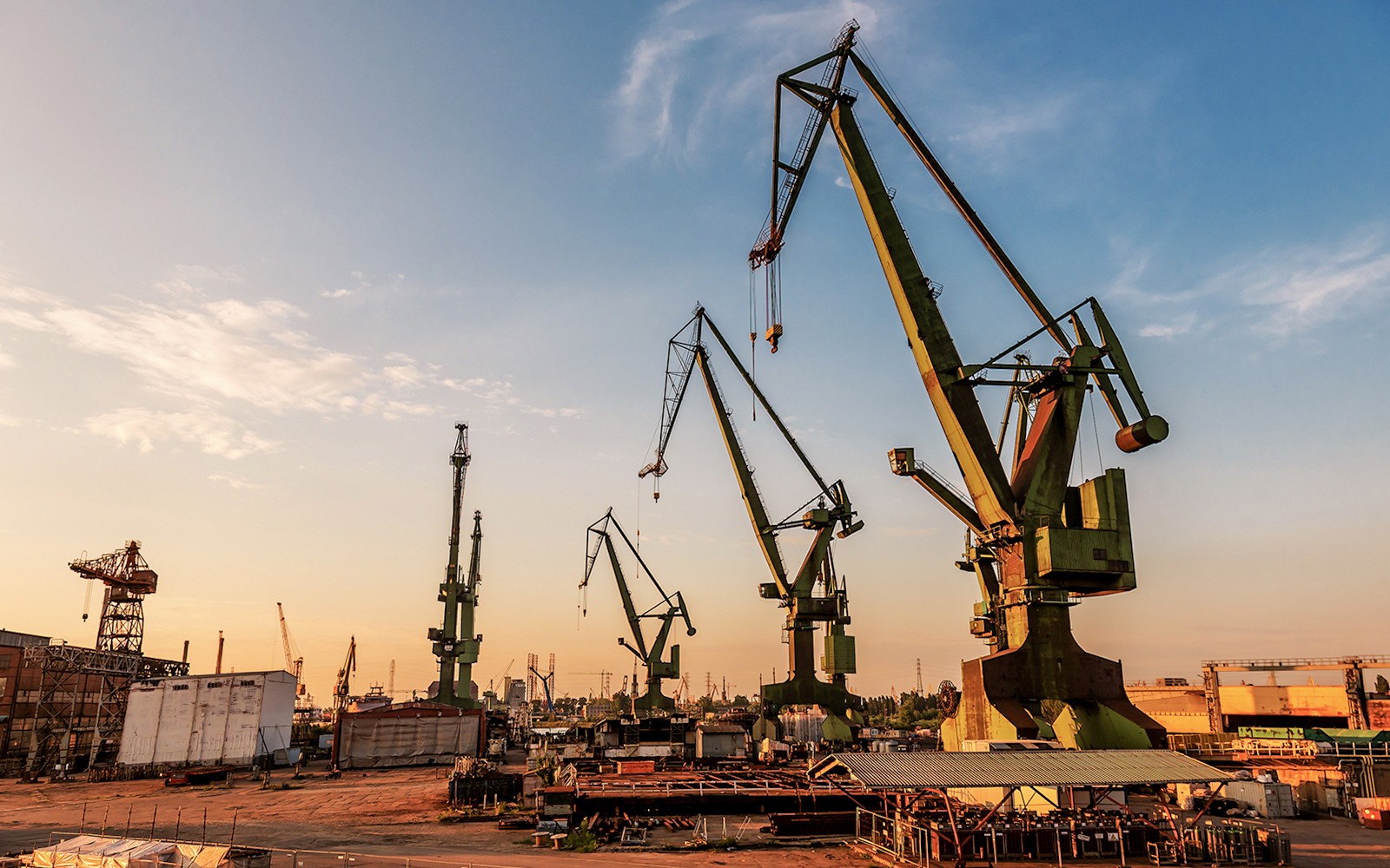 Gdansk port cranes silhouetted against a sunset sky.