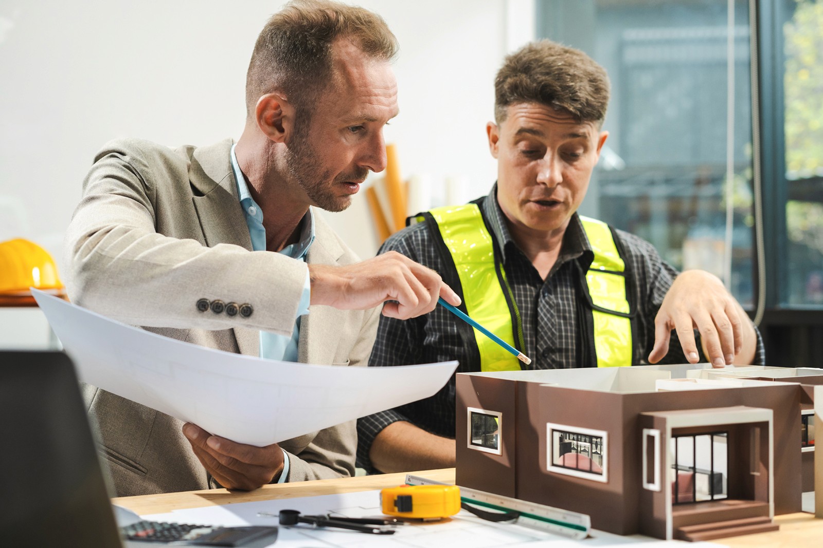 Architect en bouwheer die een maquette van een eengezinswoning bespreken.