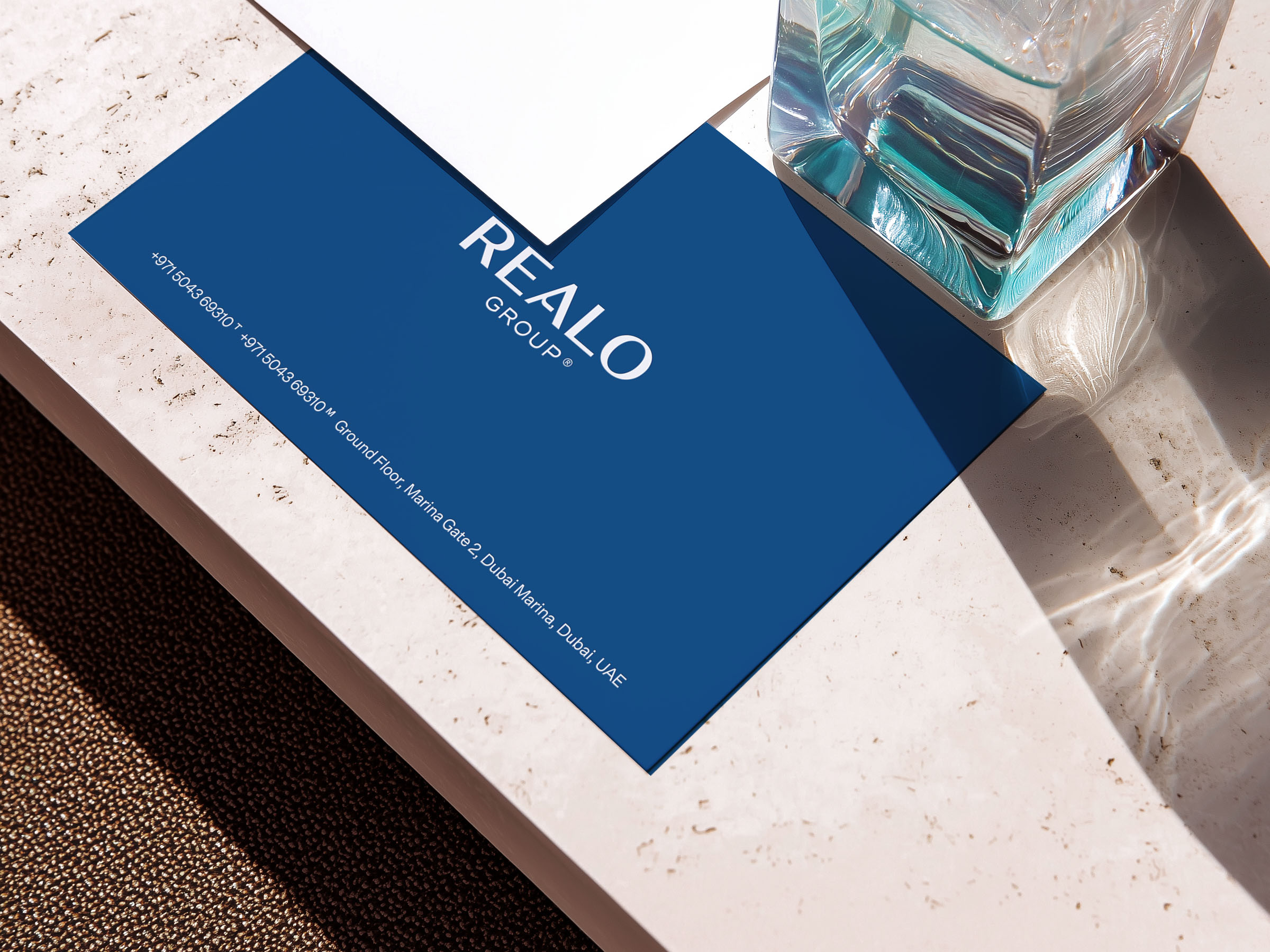 Close-up of a Realo Group stationary card on a stone surface beside a glass of water.