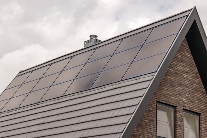 Nahaufnahme eines Hausdachs mit Solarpaneelen unter einem bewölkten Himmel.