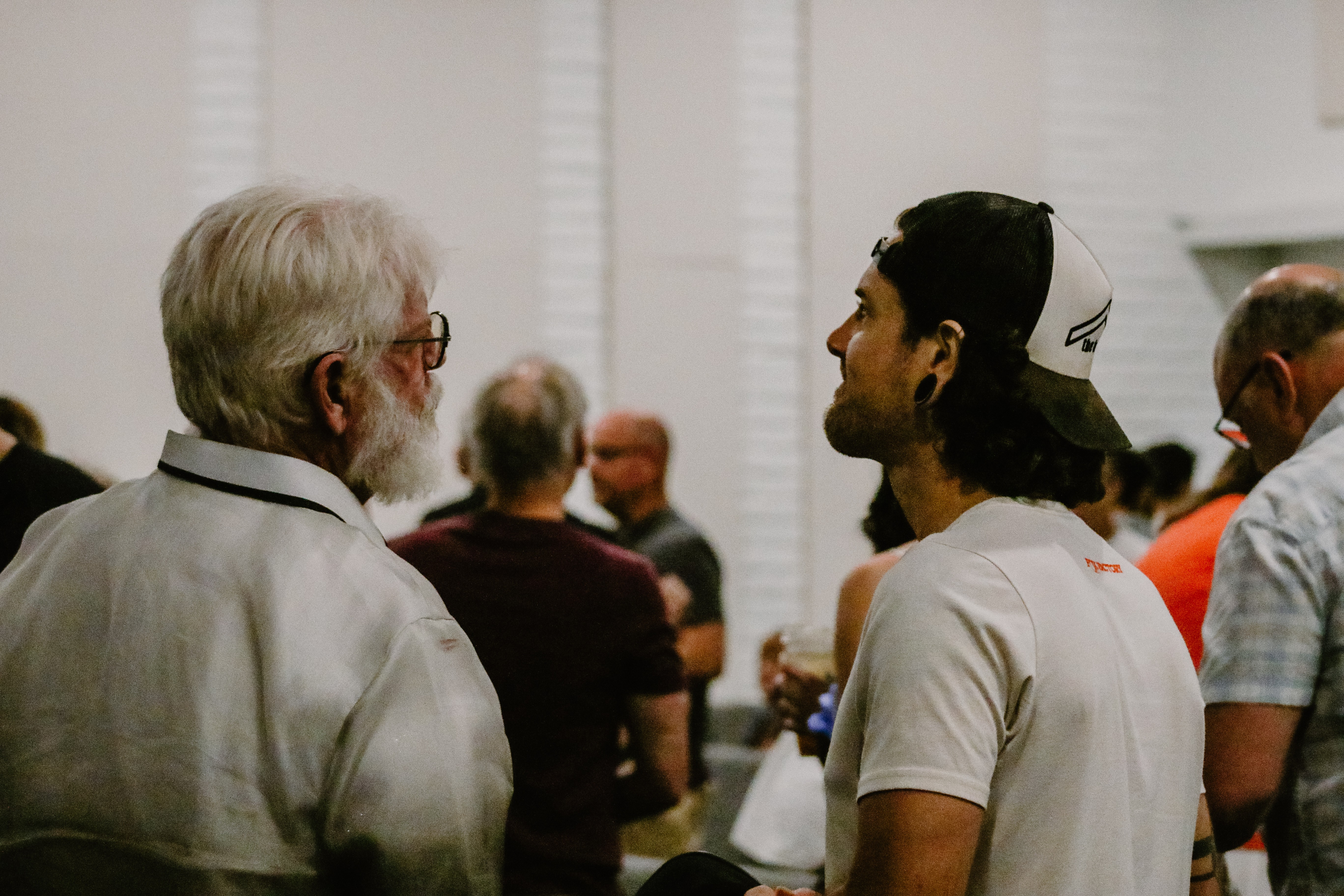 Older man and a young man in a backward cap talking in a crowded room