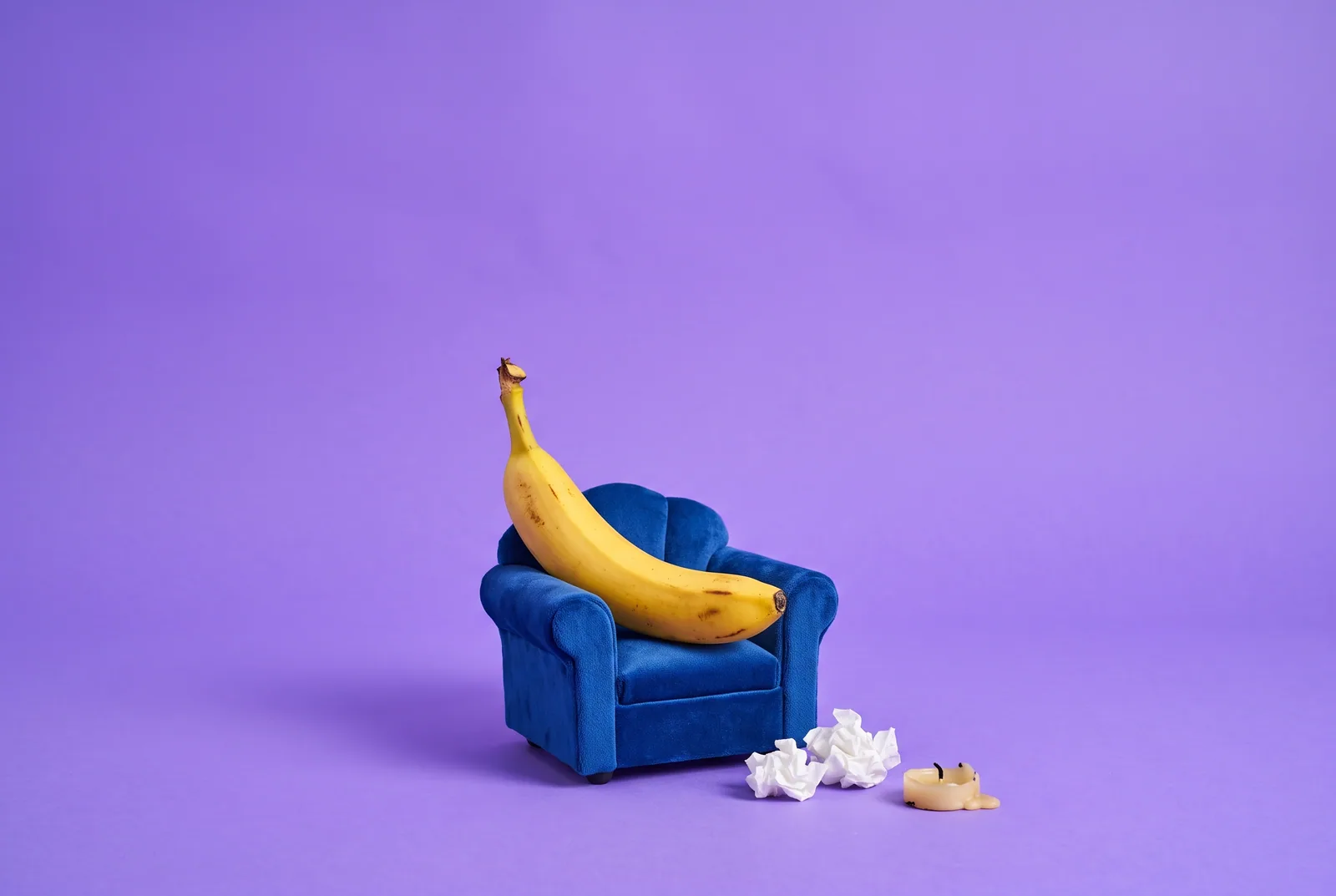 A slumped banana in an armchair beside tissues and a burned-down candle, signs and symptoms of gooning addiction