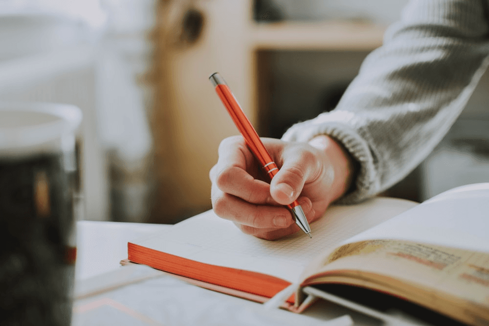High school student writing a thesis at a desk with research notes and academic books