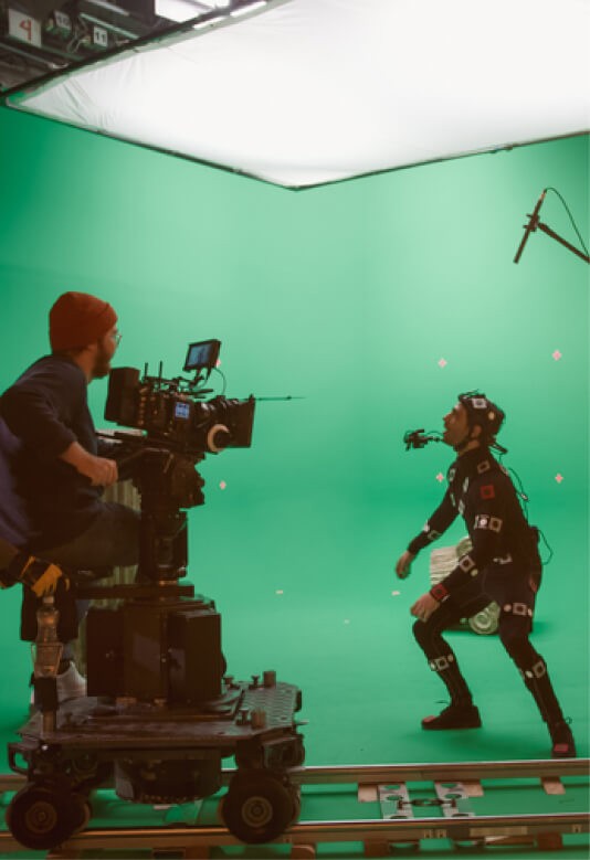 A camera operator films a performer in motion against a green screen backdrop.