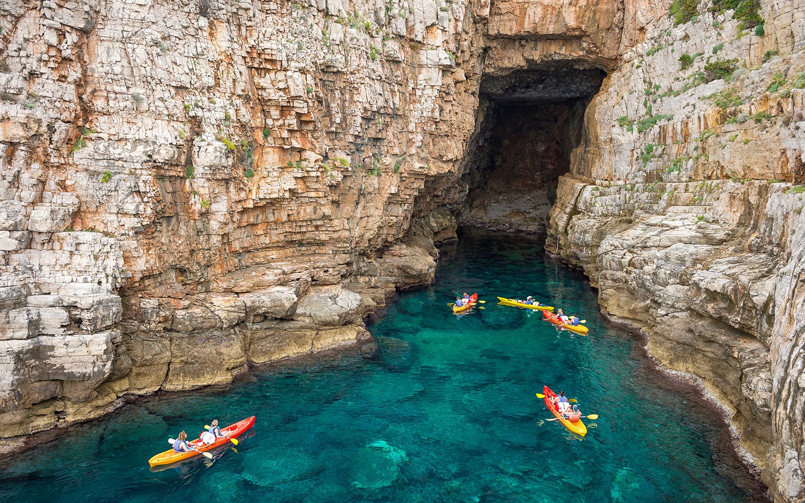 Kayakers exploring sea cave near rocky cliffs in Dubrovnik.