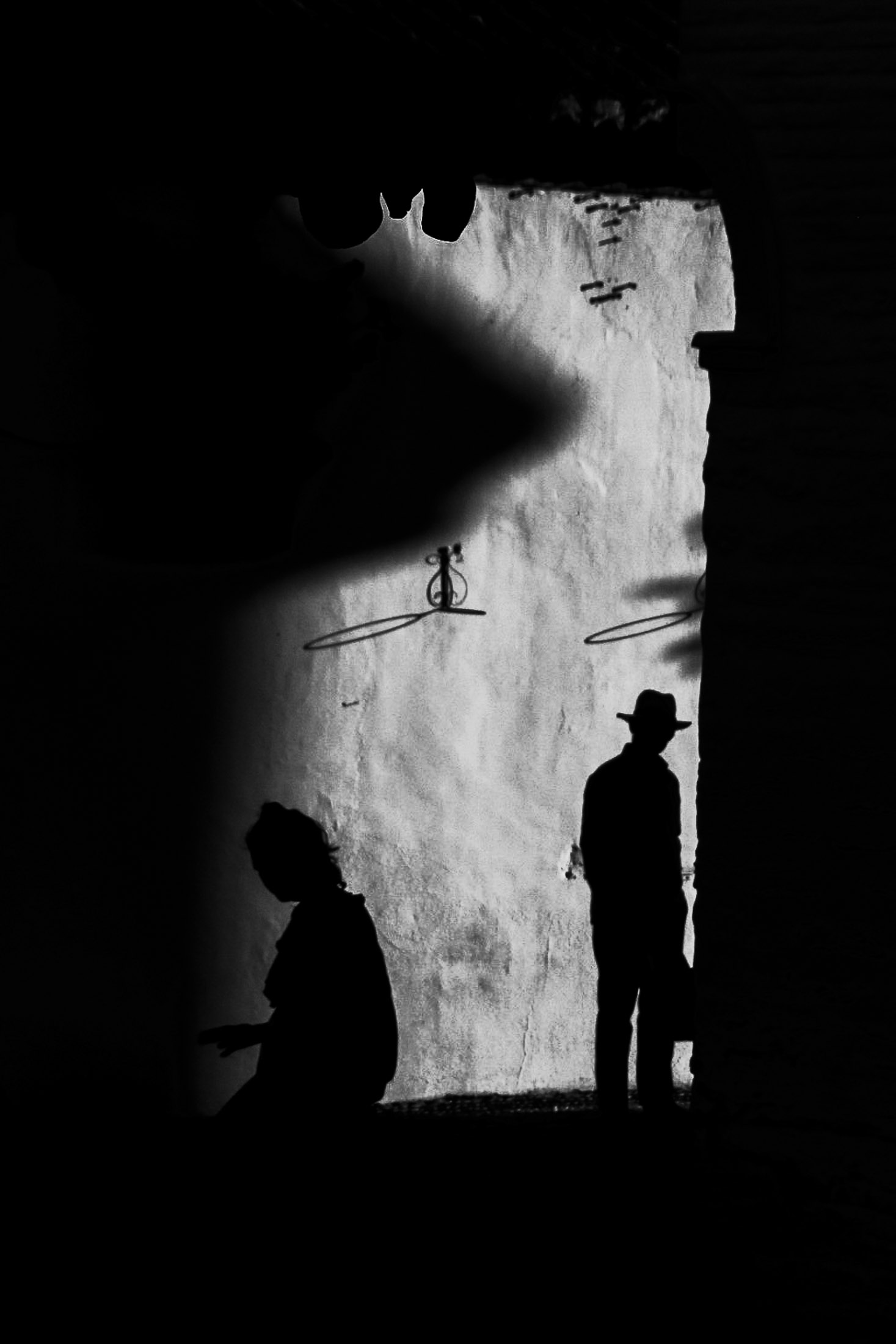 Black and white photograph of two silhouetted figures standing against a textured wall in dramatic light. 9
