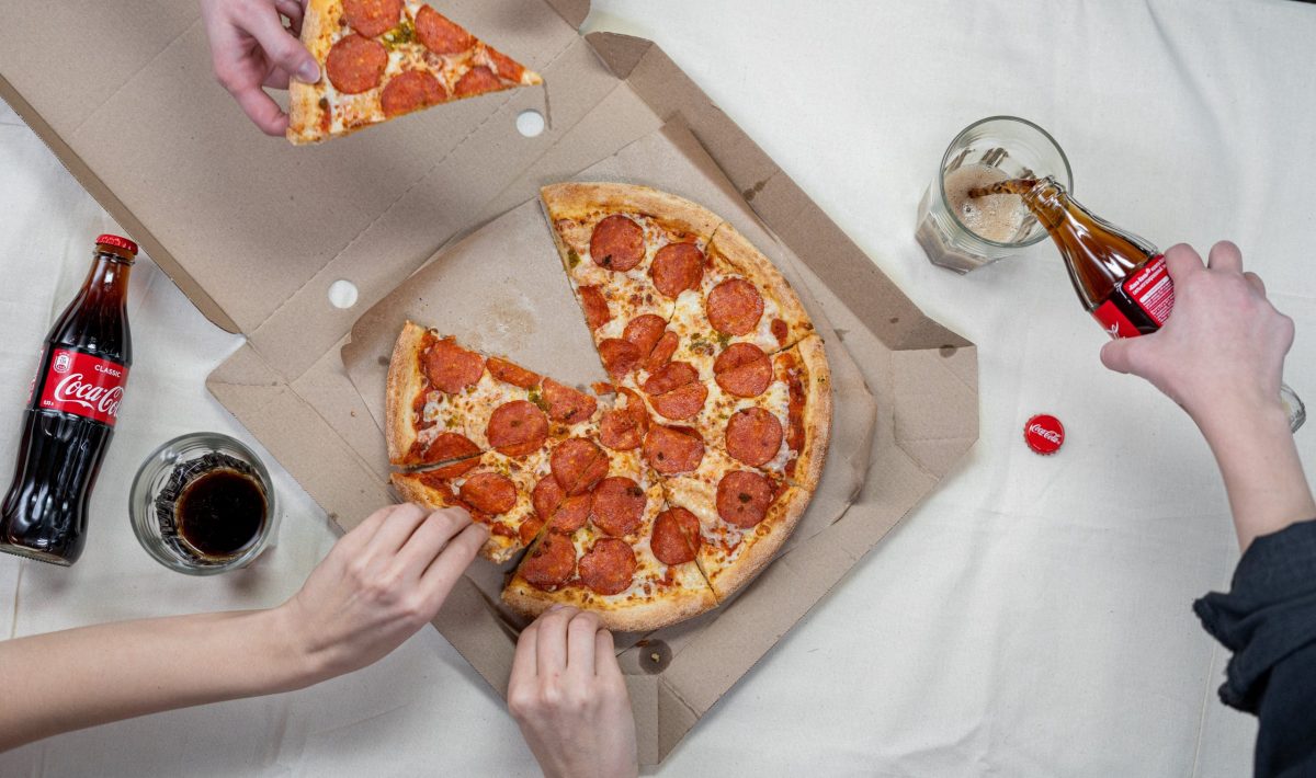 Aerial shot of hands grabbing pizza and pouring cola drinks.