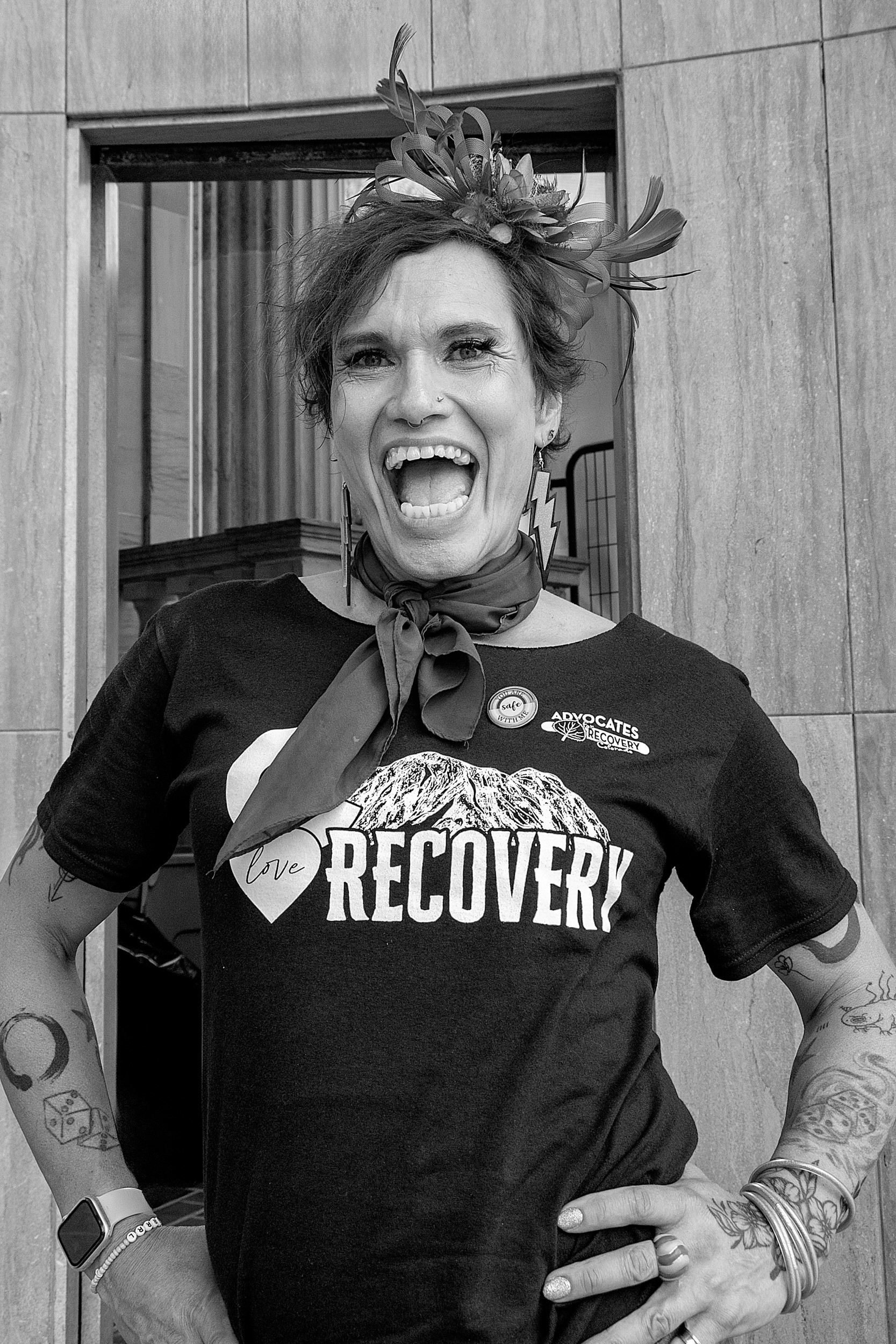 Person with expressive tattoos and a bandana grinning wide, wearing a “Recovery” shirt and standing confidently