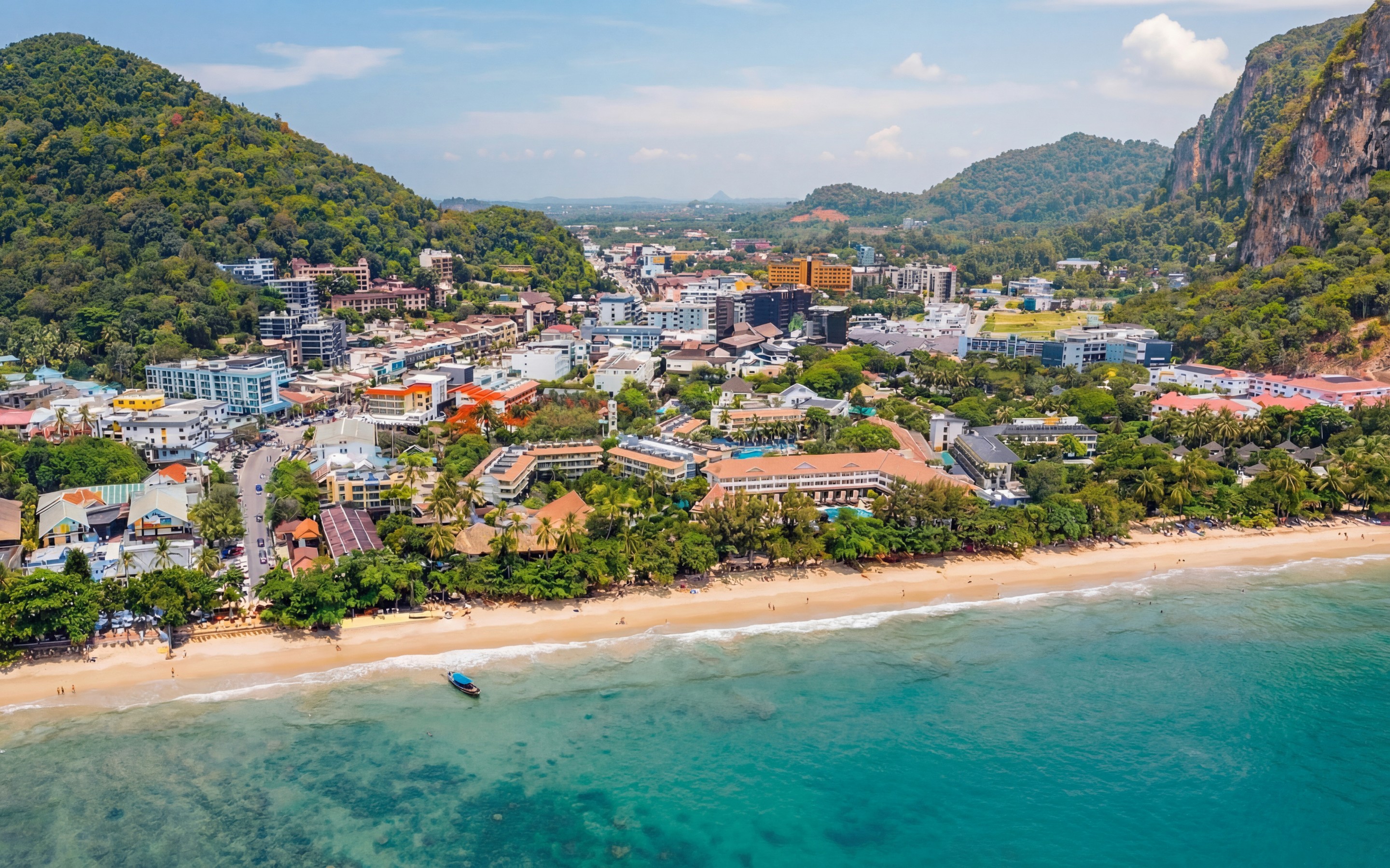 Aerial view of Ao Nang beachfront and town centre, with low-rise buildings set between the beach and surrounding hills.