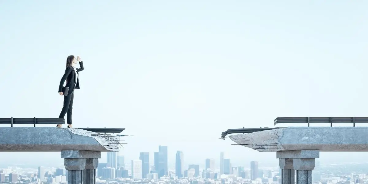 A man stands while two people sit at a table in an office setting, smiling and engaged in conversation. The mood is friendly and collaborative.