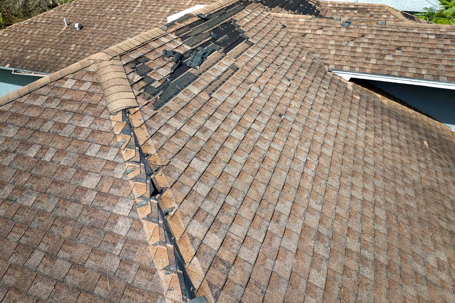 Wind damaged house roof with missing asphalt shingles after hurricane Ian in Florida Repair of home rooftop concept