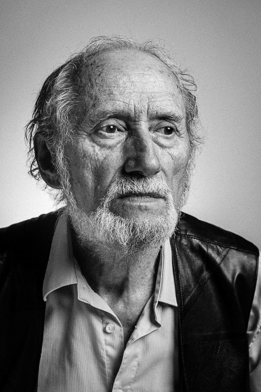 Portret starszego mężczyzny z siwą brodą, ubranego w koszulę i fular.