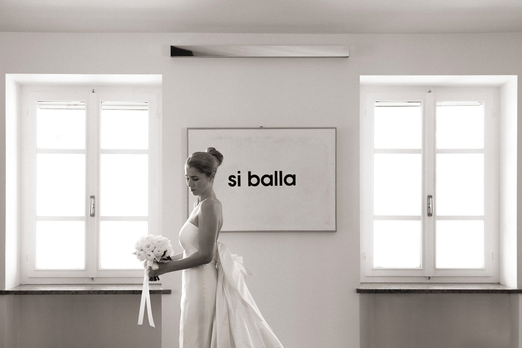Sposa in abito bianco con bouquet davanti a scritte murali in stanza luminosa a Villa Malenchini