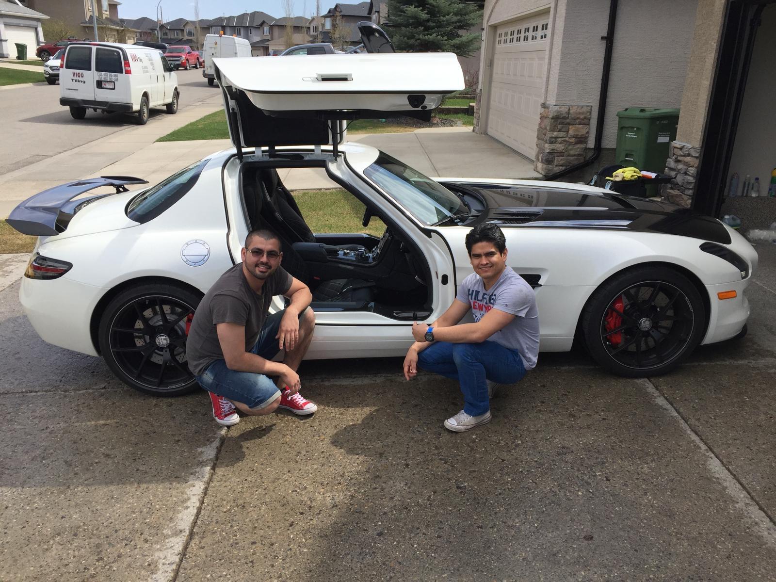 Two men squatting beside a white gullwing car.