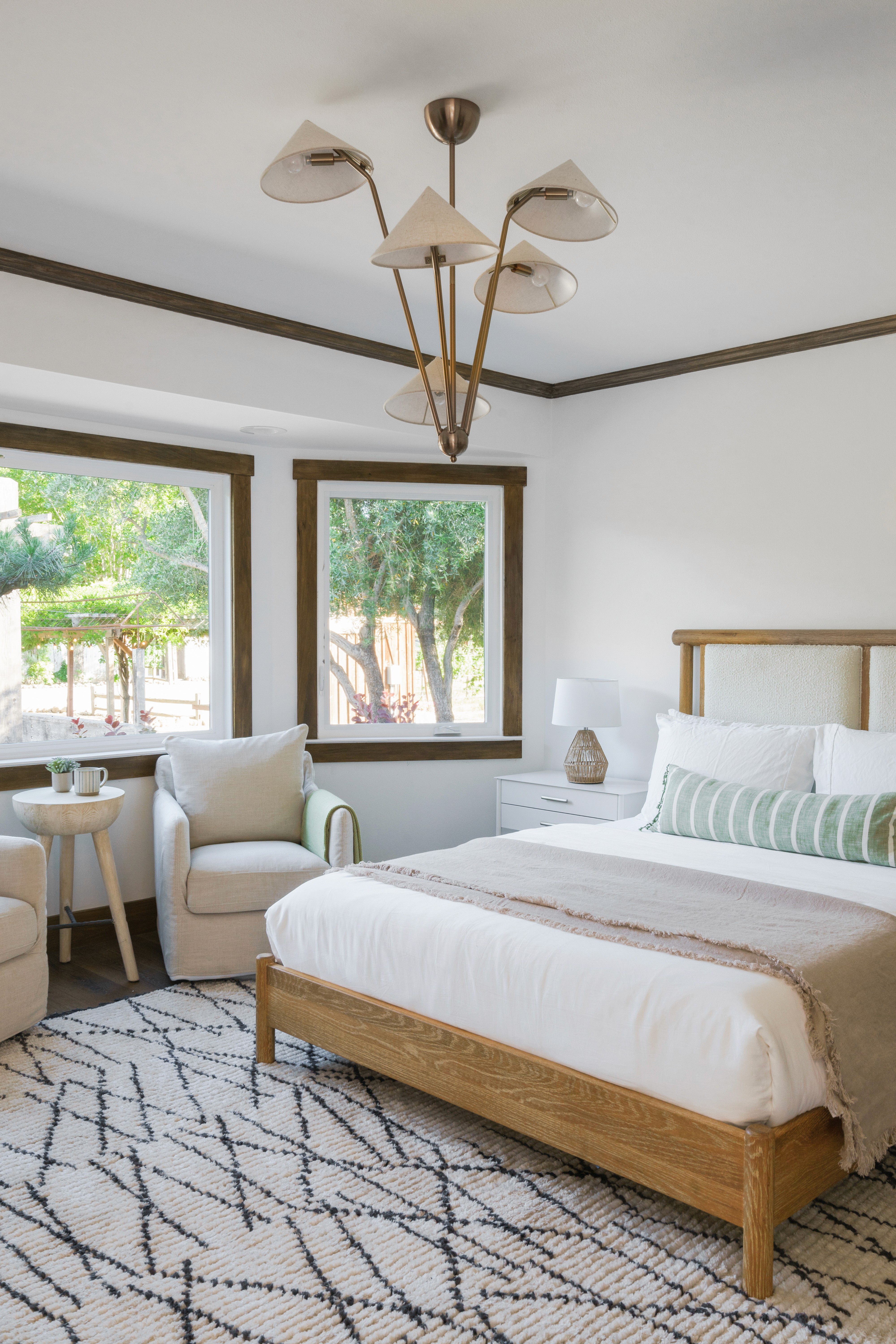 This landscaped outdoor retreat blends East Coast charm with Southern California sunshine, featuring a cozy patio, an eight-person wooden dining table, and rattan light fixtures for a warm, inviting ambiance