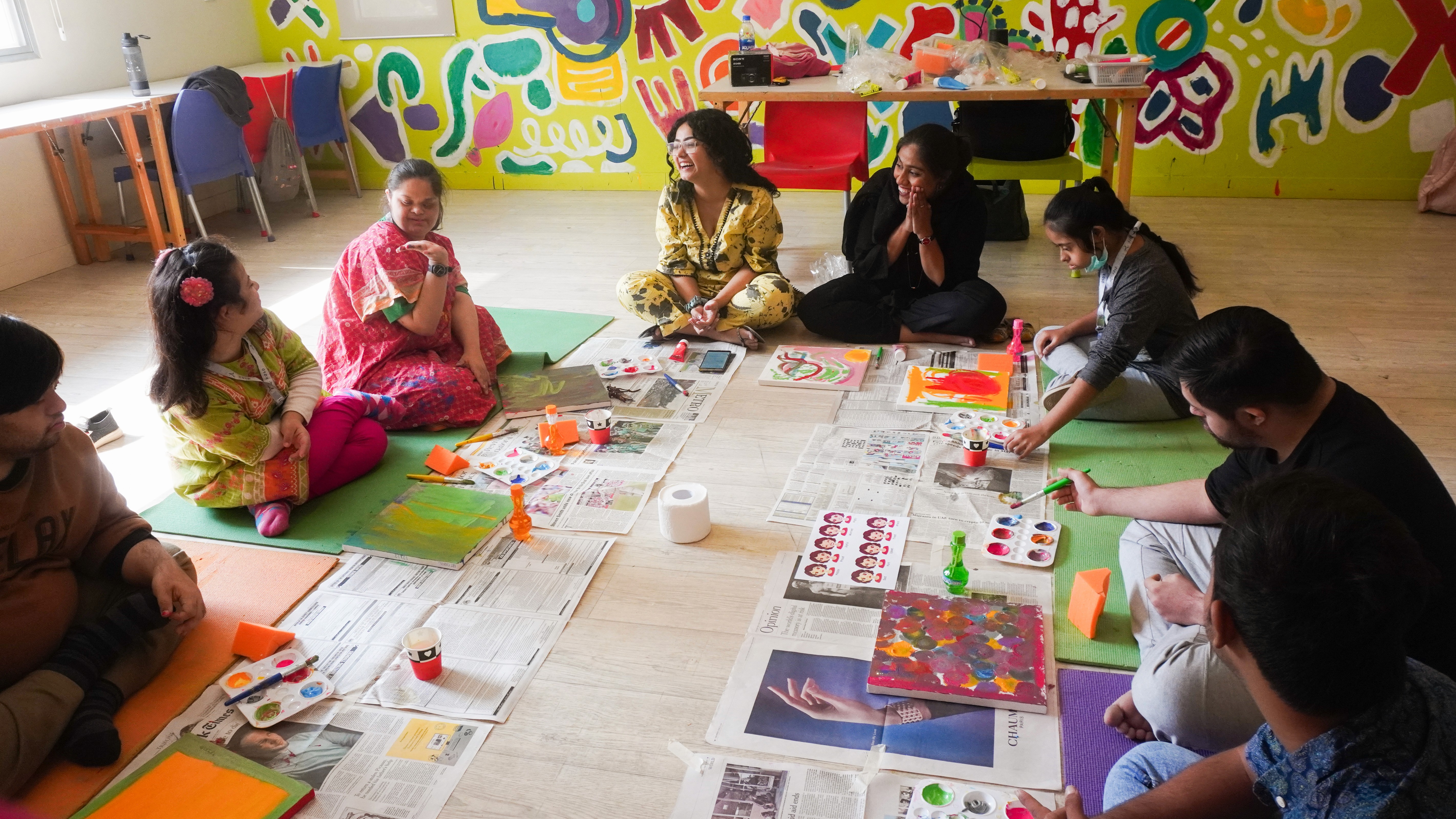 A group of children with down syndrome creating artwork sitting around art supplies