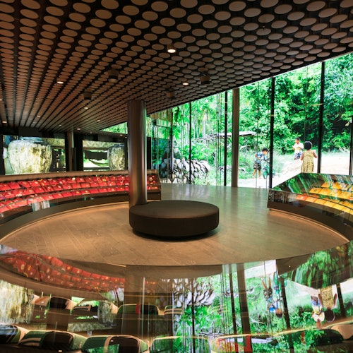 A modern, circular indoor space with large digital screens displaying nature scenes and cushioned benches around the perimeter.