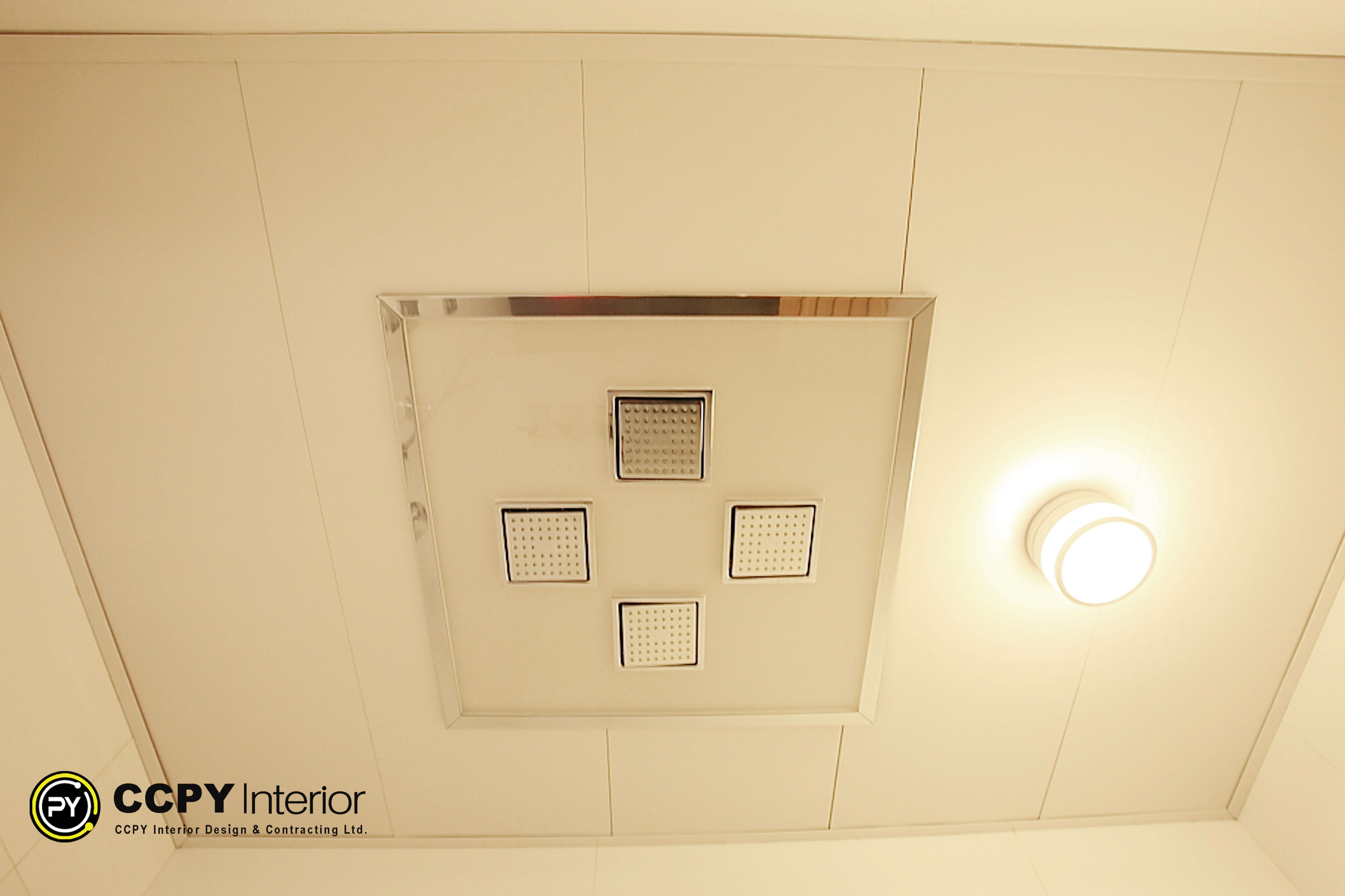 Ceiling-mounted square rain shower heads and minimalist circular lighting integrated into a white bathroom ceiling at Standalone House, Perkins Road.