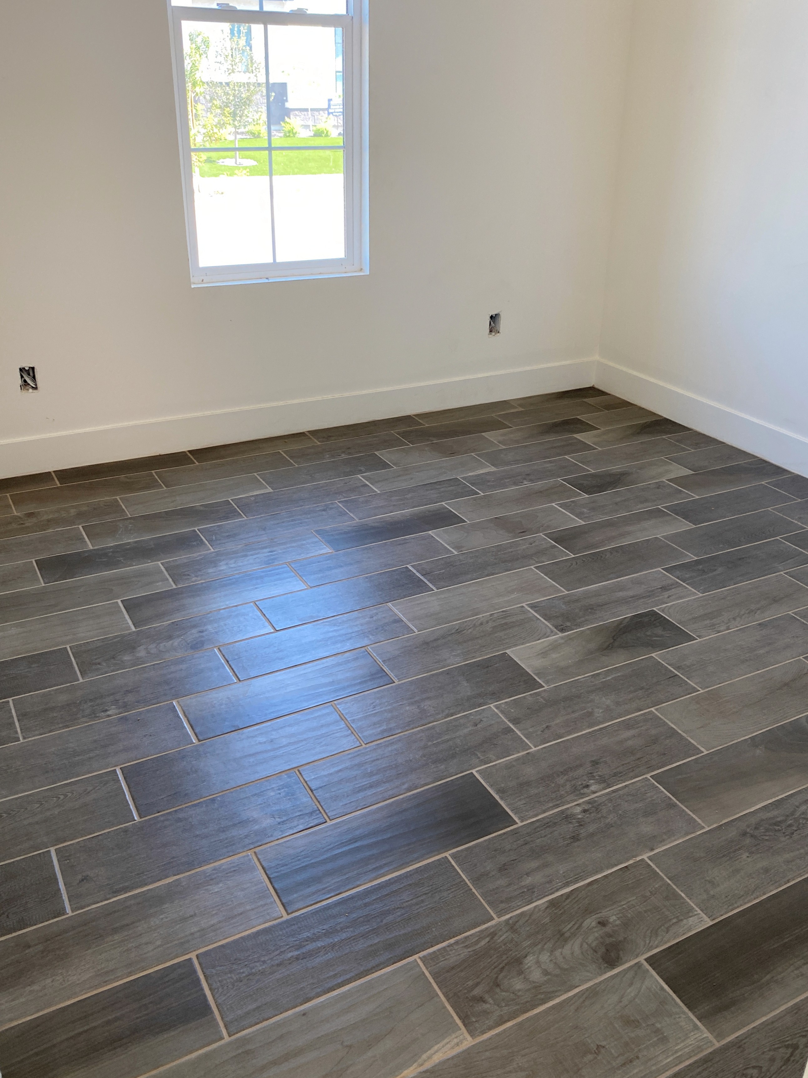 Modern living room with glossy gray wood-look tile flooring and large windows in a new home under construction.