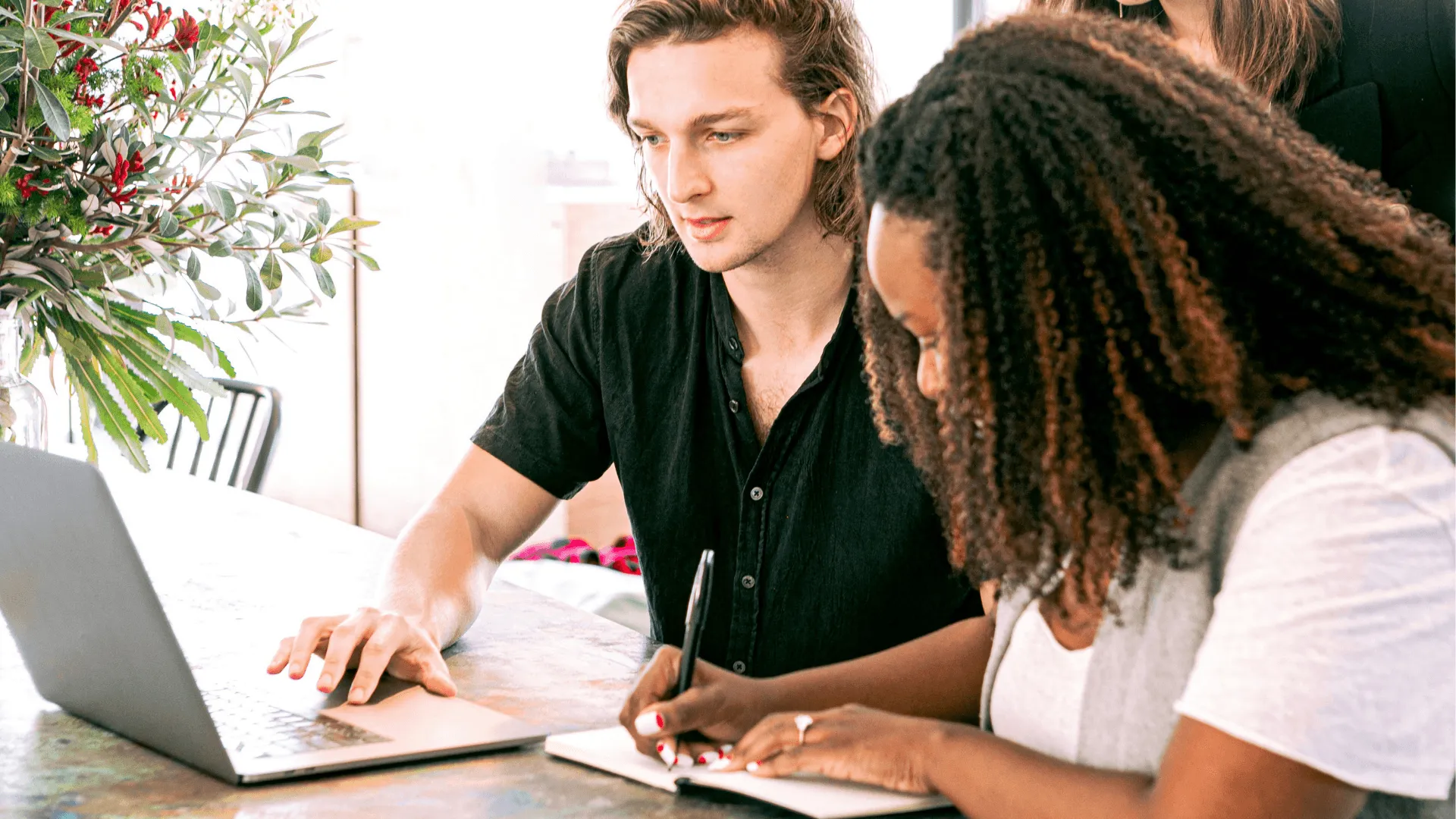 Two people working together, one on a laptop while the other takes notes in a notebook