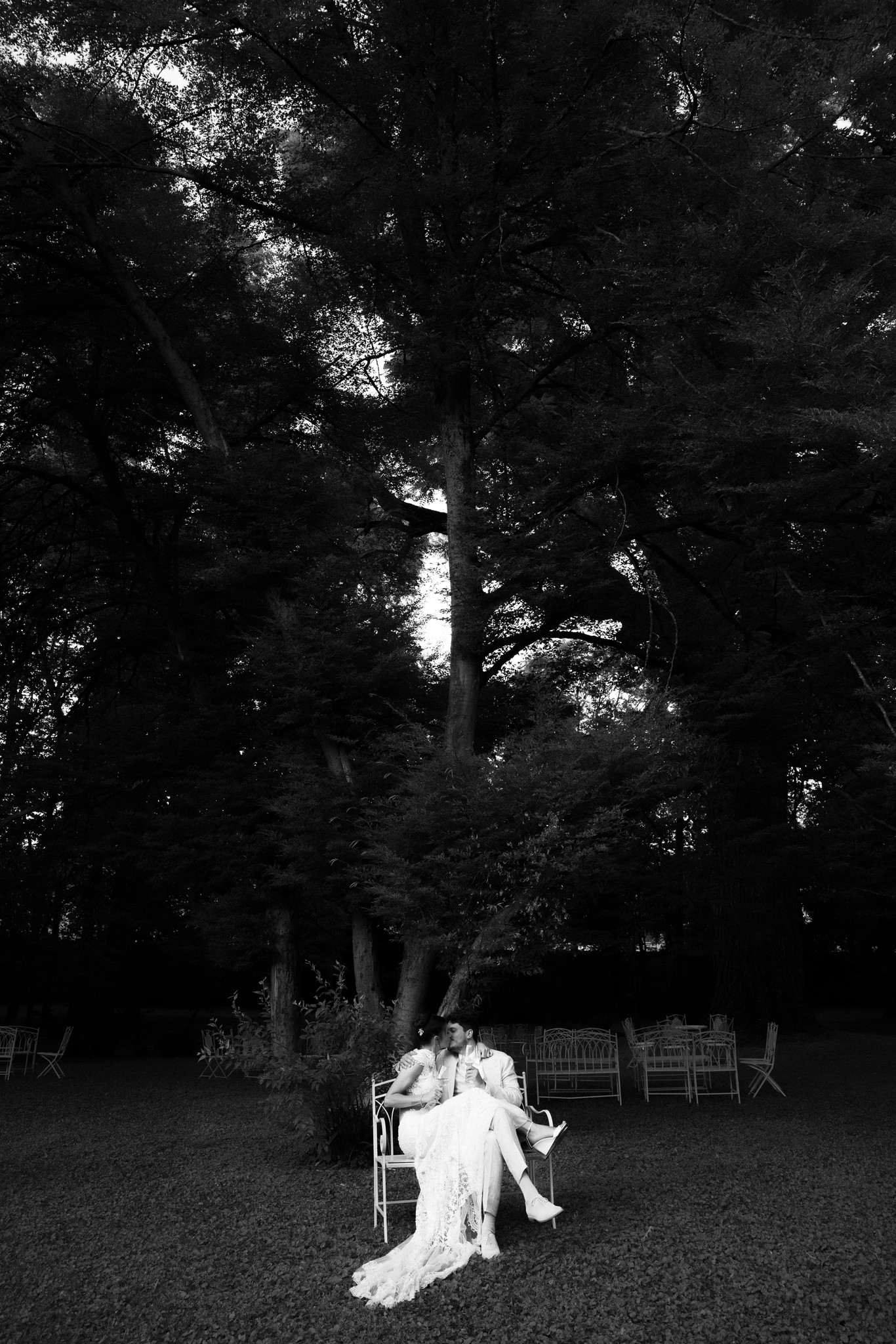 Sposa seduta su sedia in giardino sotto alti alberi, reportage di matrimonio alla Rocca di Soragna in bianco e nero