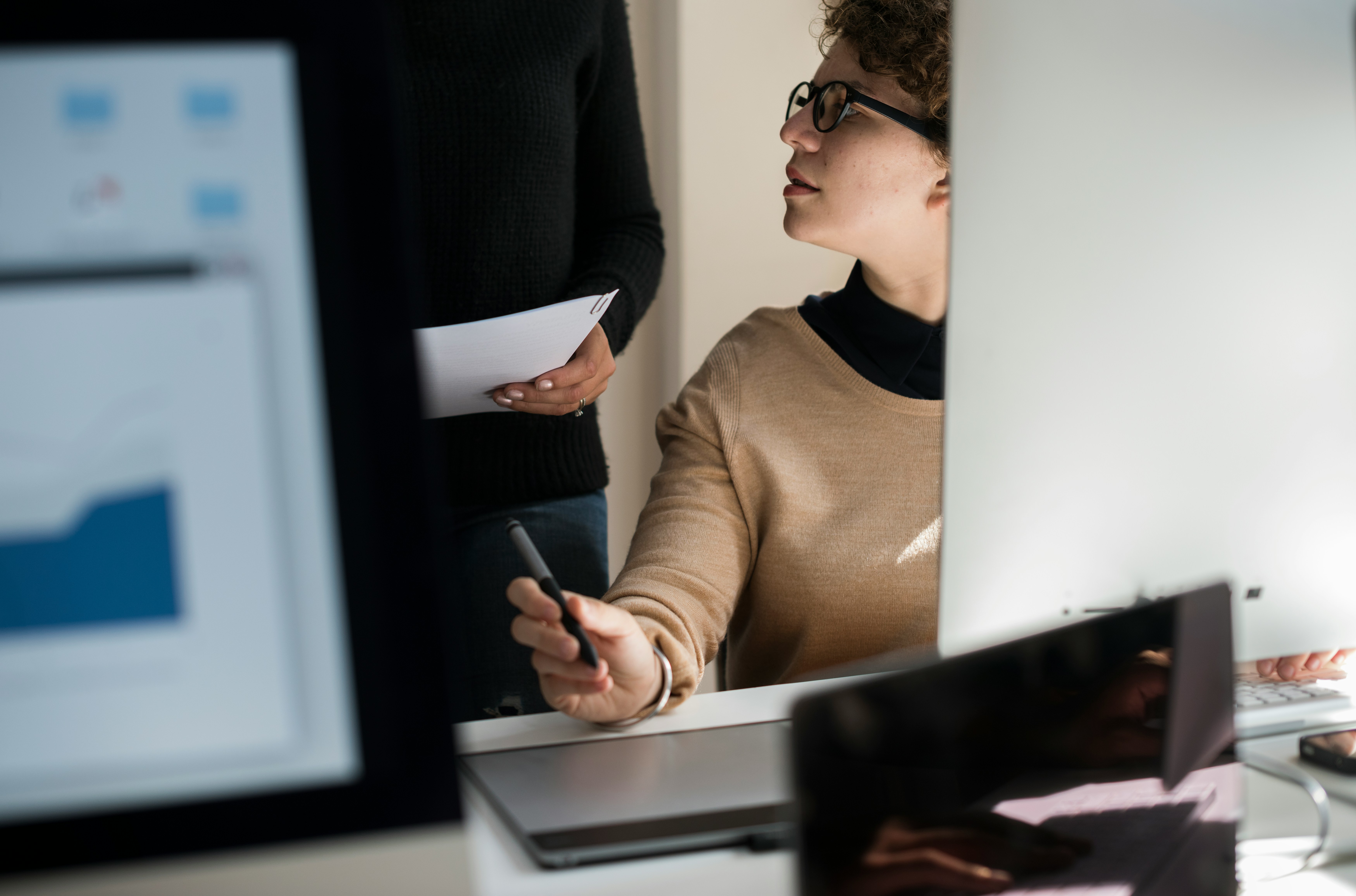 Female business professional at desk engaing in conversation with colleague