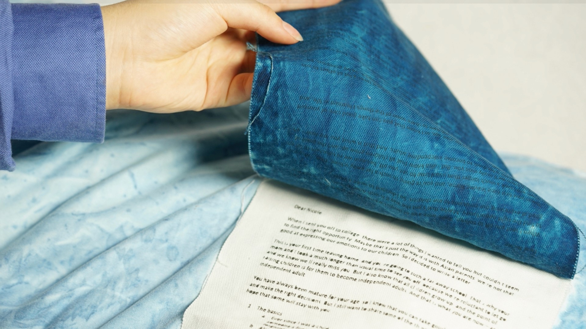 a hand lifting a cover to show a letter. the letter is resting on a pillow.