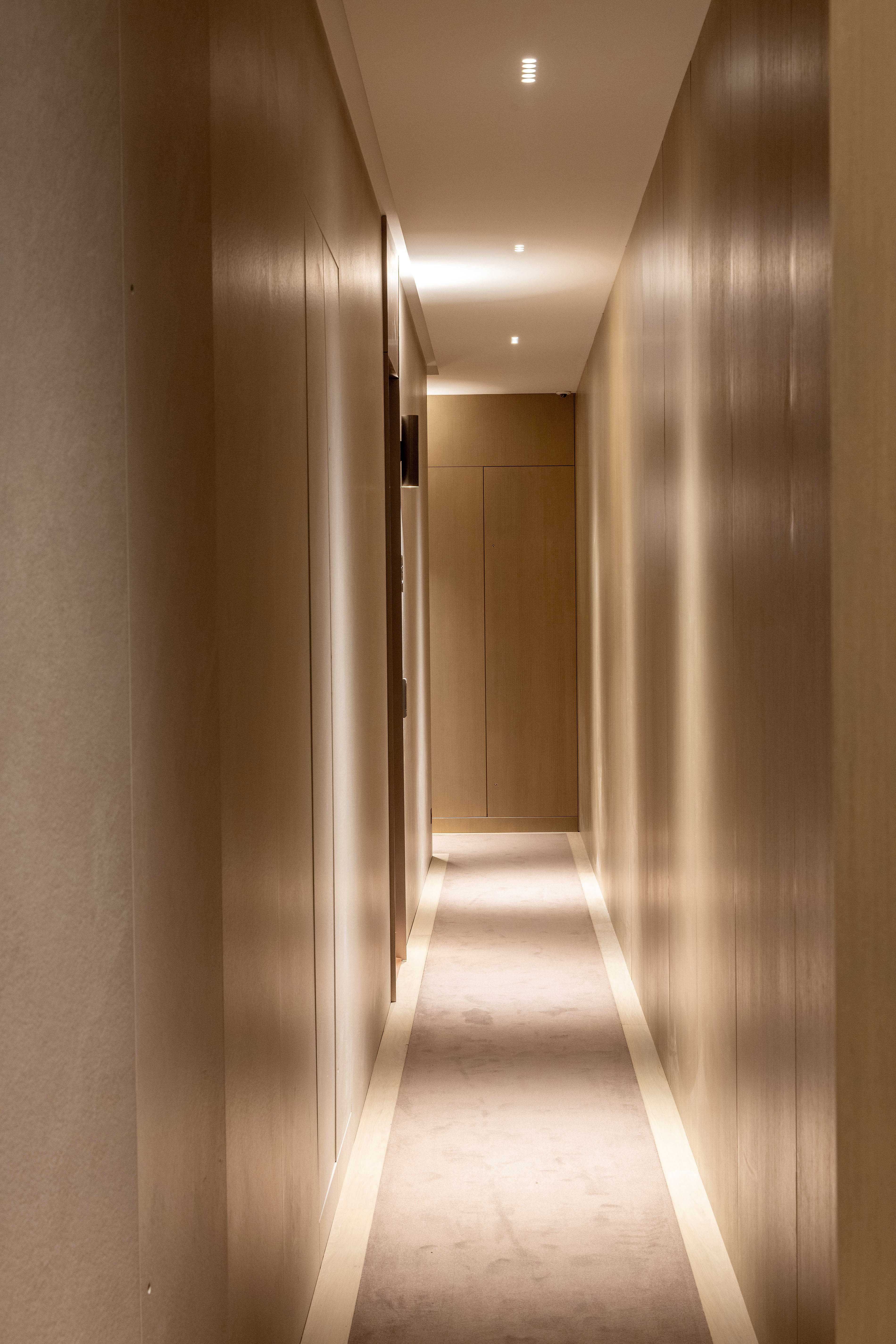 Couloir d'étage en bois clair avec moquette beige, éclairage encastré et bandes lumineuses au sol