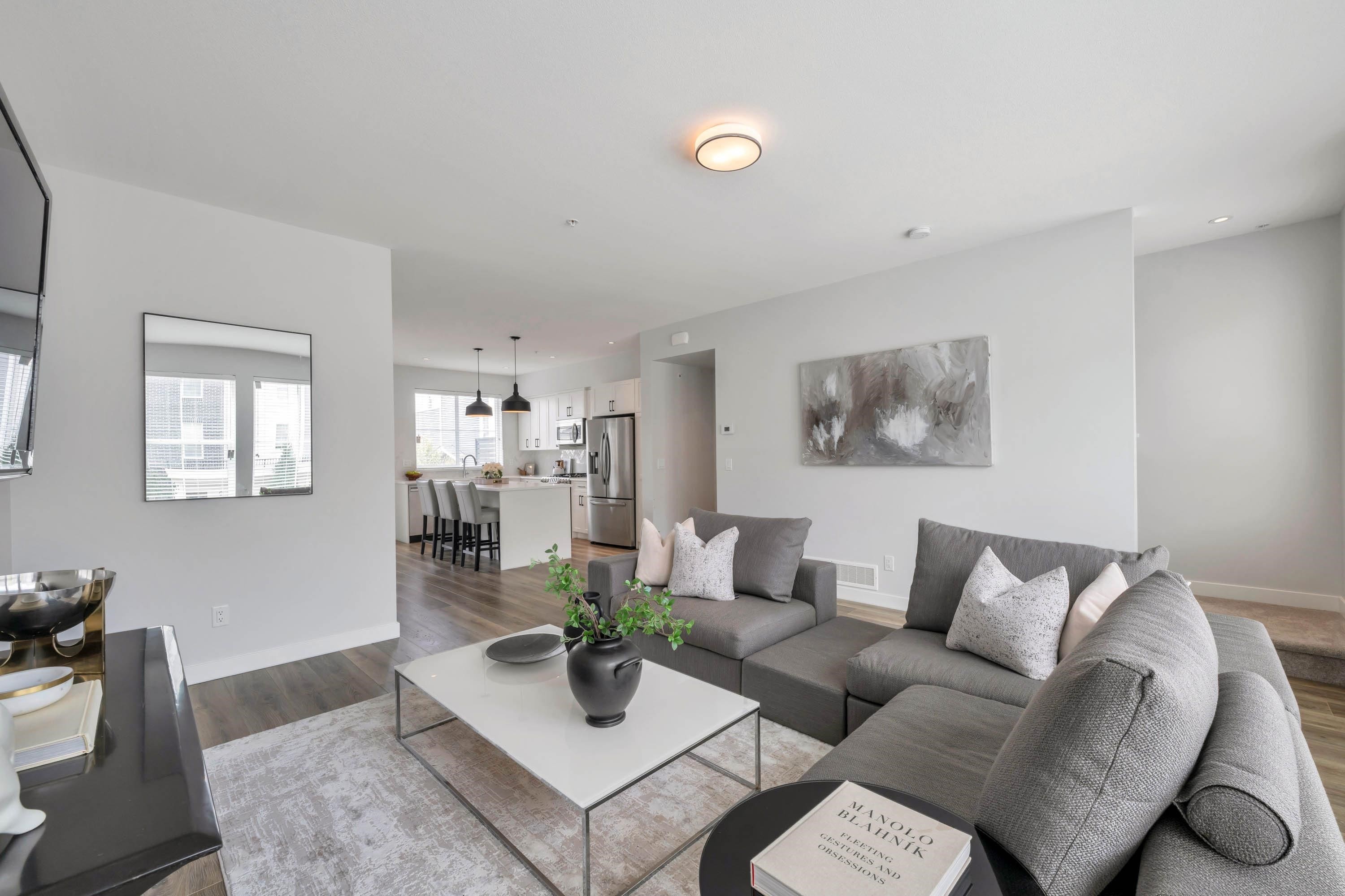 Modern living room featuring gray furniture, a coffee table, decorative plants, and ample natural light.