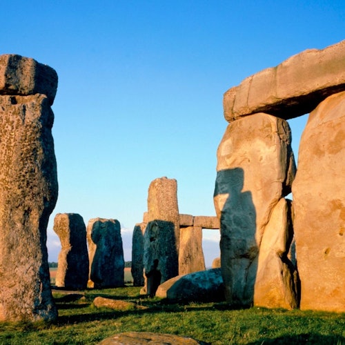 Large stone monoliths forming a circle on grass, under a clear blue sky, likely part of an ancient structure.