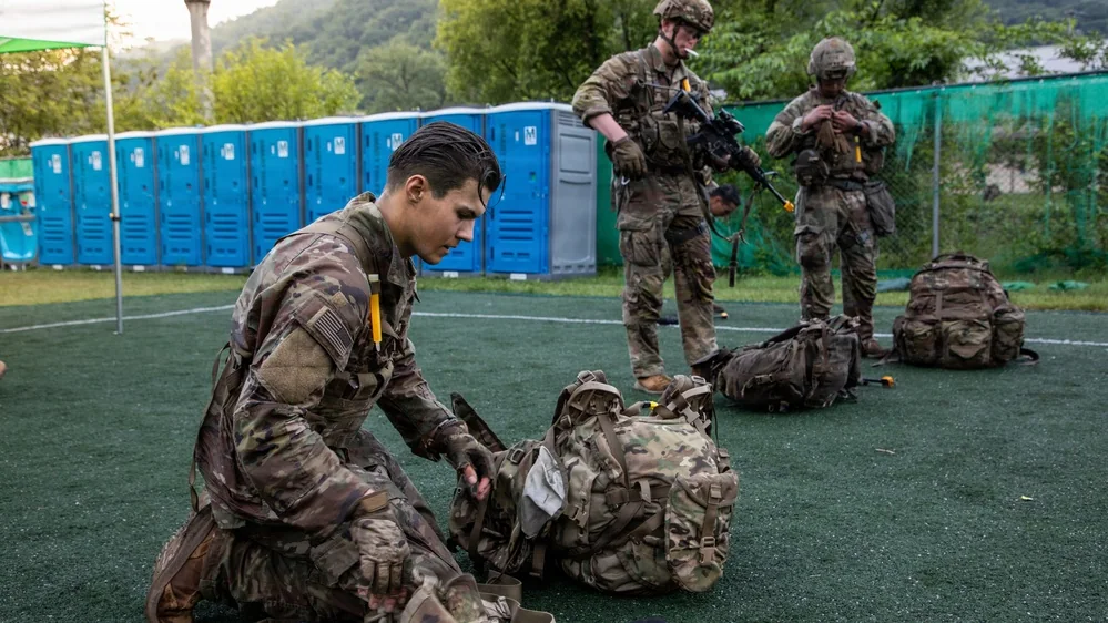 Soldier kneeling beside his MOLLE II rucksack, packing it before a ruck march