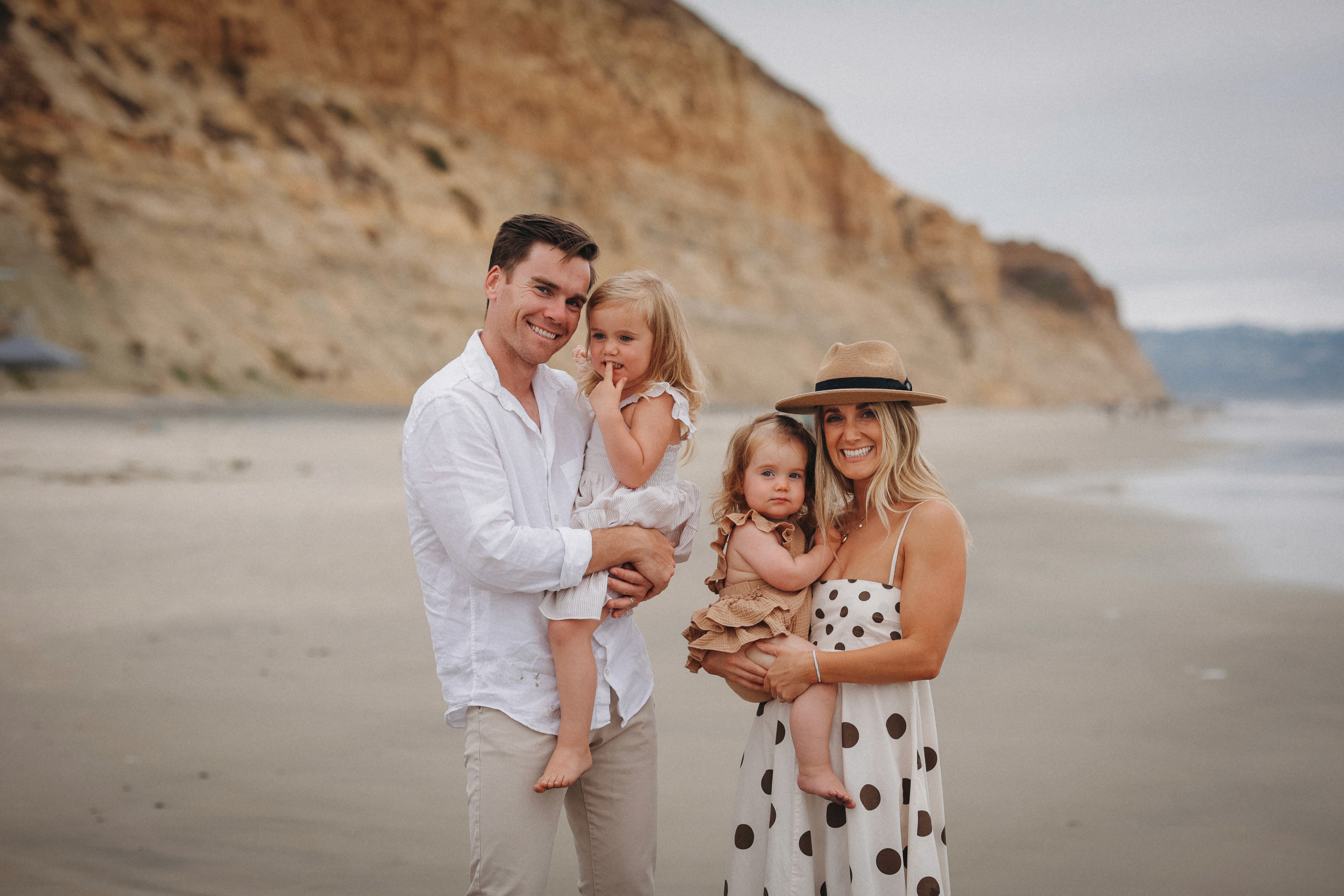 Family standing together on the beach near sandstone cliffs during a candid lifestyle session