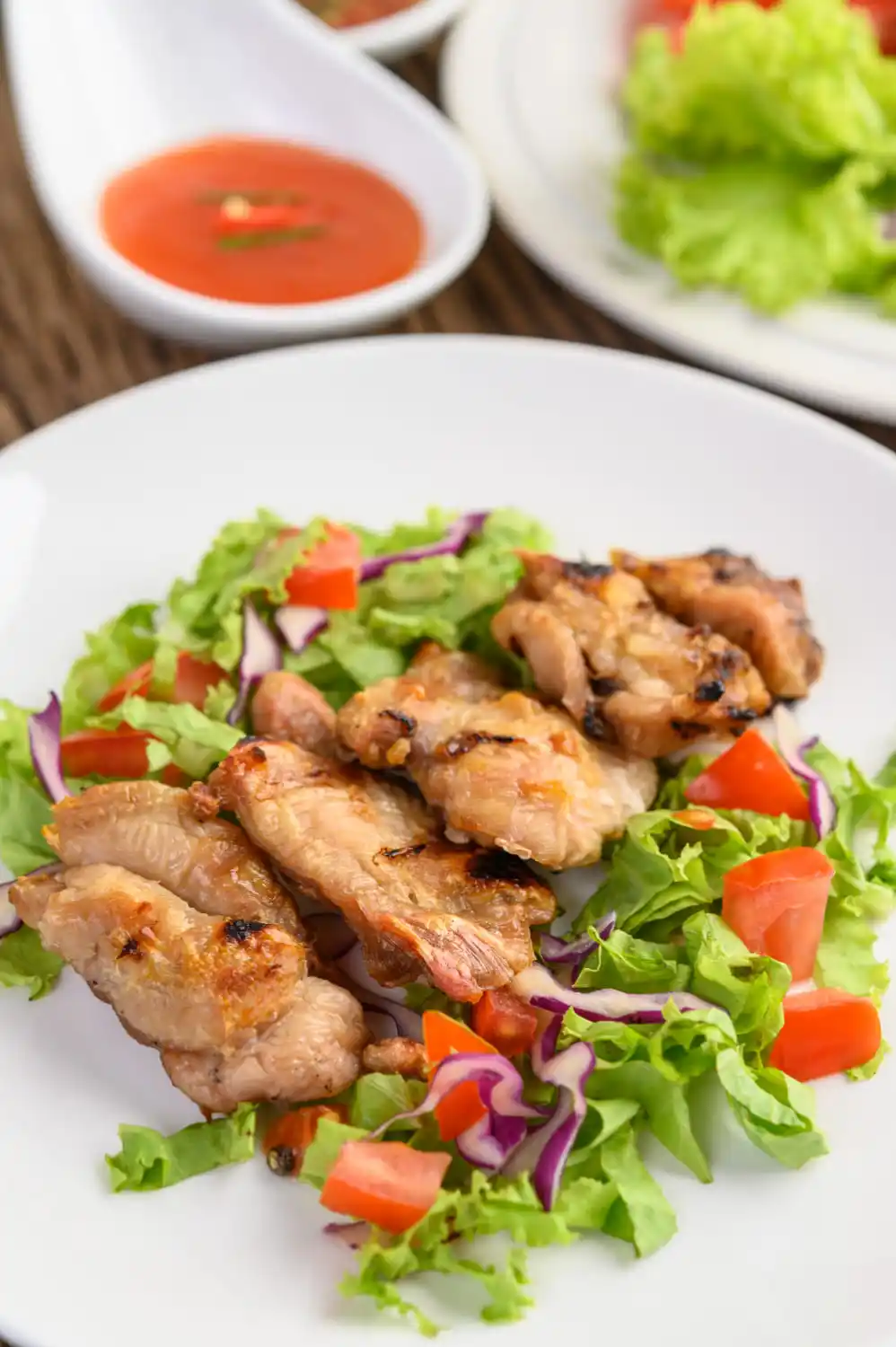 Grilled chicken pieces on a bed of fresh green salad with tomatoes.