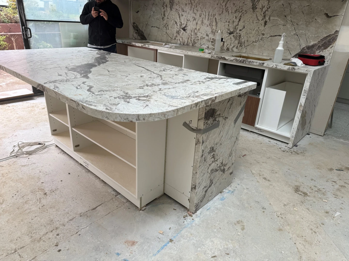 Natural stone kitchen island installation in progress with marble benchtop, cabinetry, and site protection.