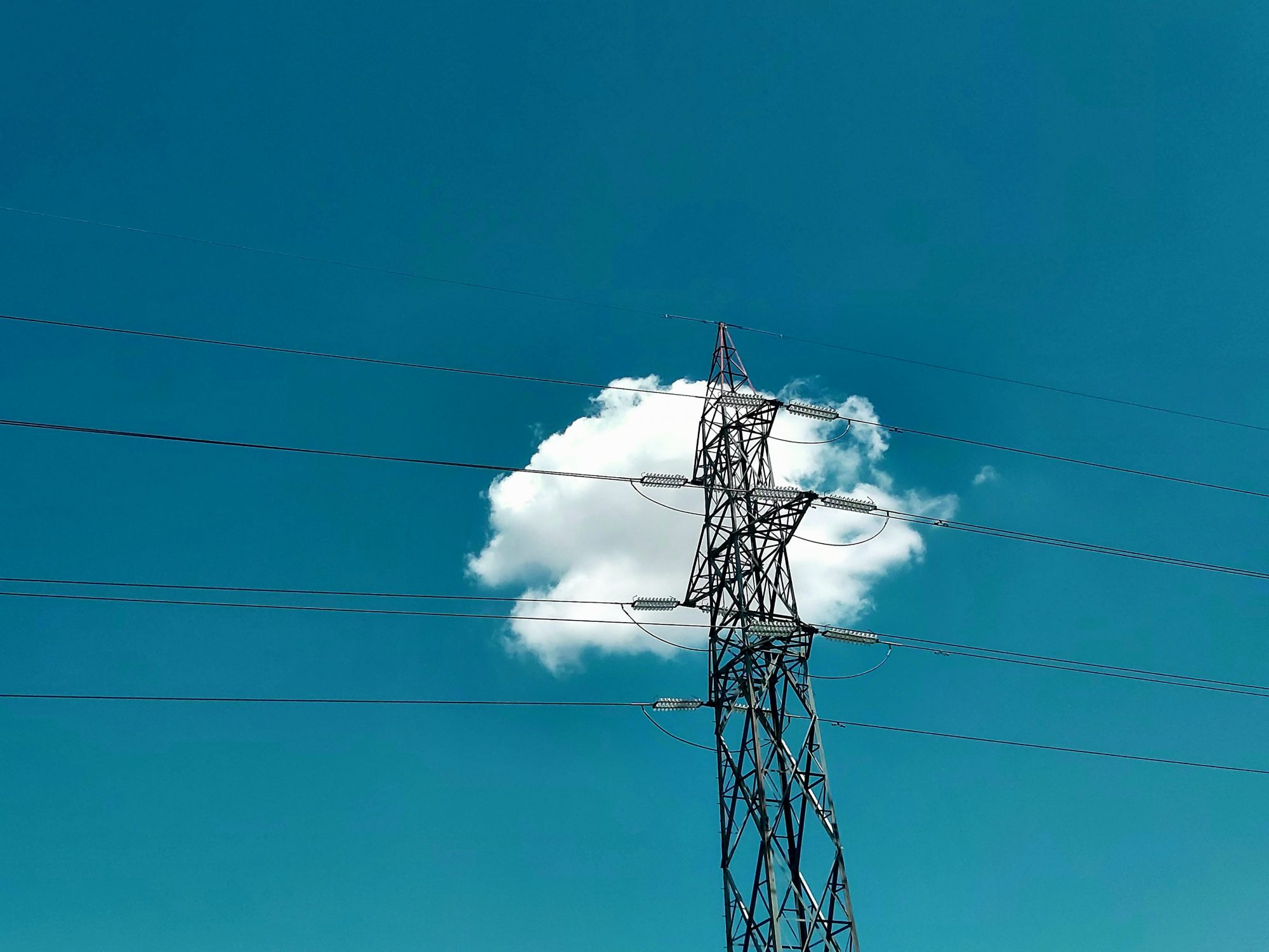 A wind turbine against a bright blue sky, with a fluffy white cloud partially obscuring it.