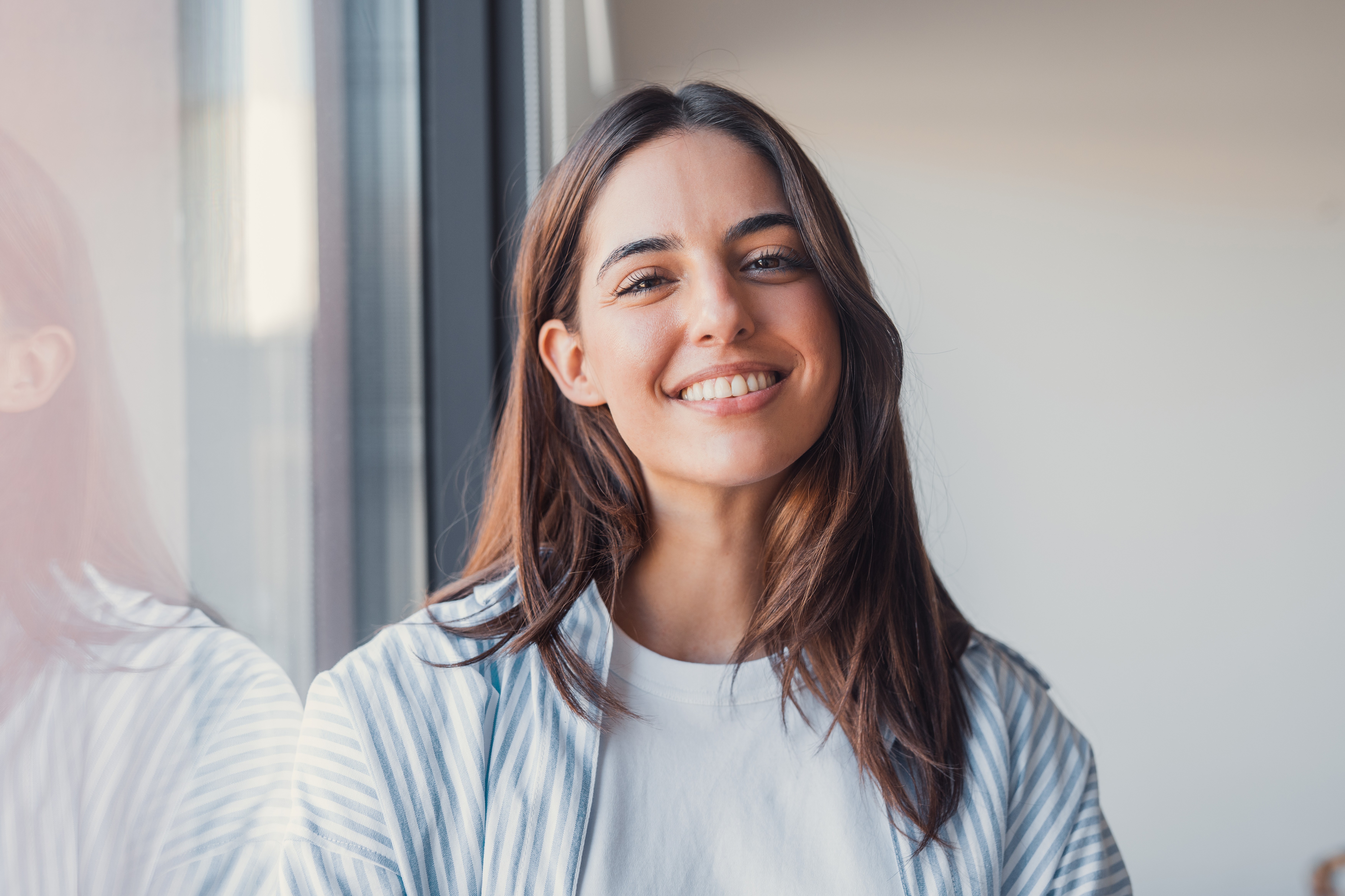 A young woman with long brown hair smiles warmly against a green background, dressed in a black jacket and white shirt.