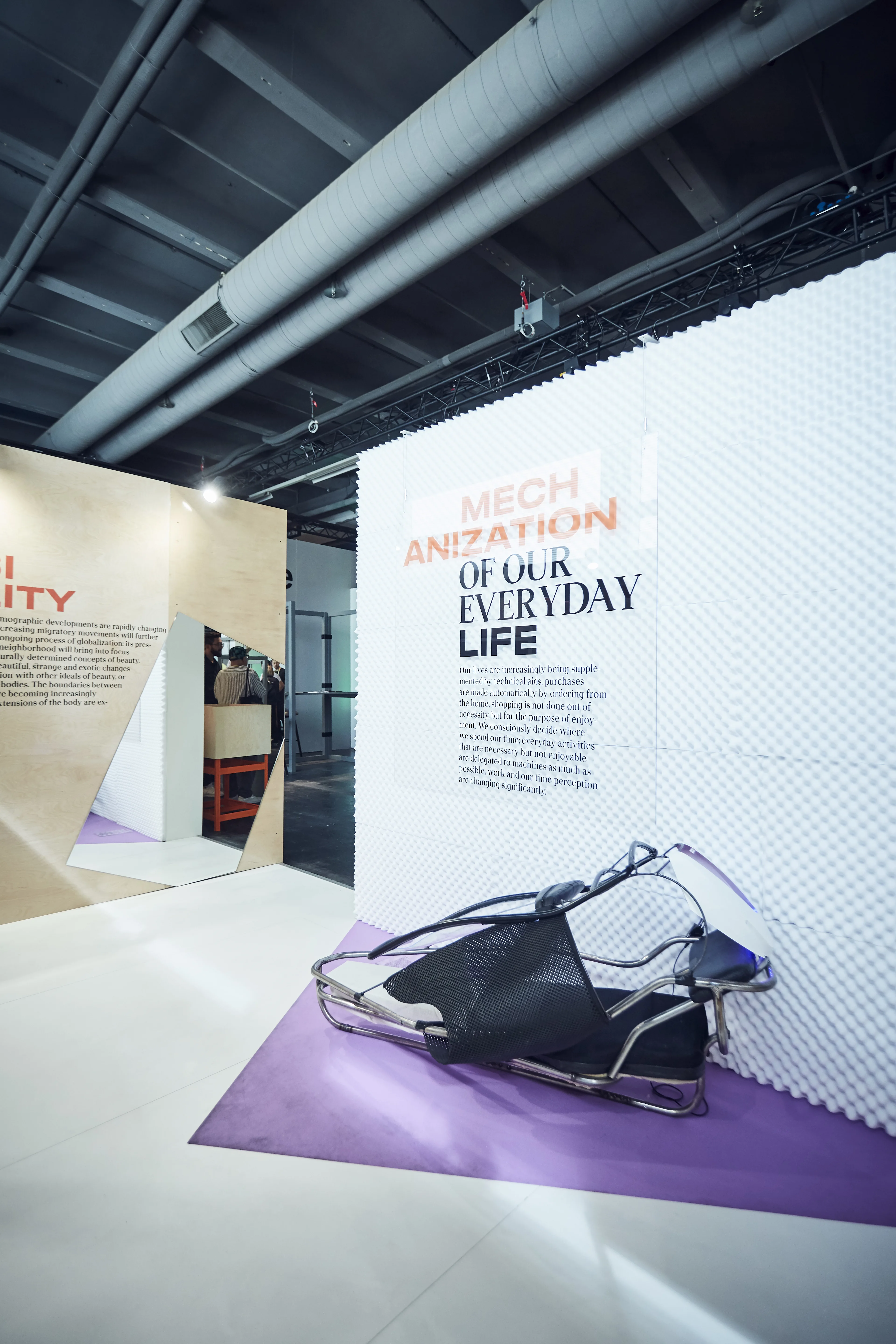Entrance area of the Cosnova exhibition with white acoustic-foam wall, Mechanization of Our Everyday Life lettering and a futuristic object on purple flooring.