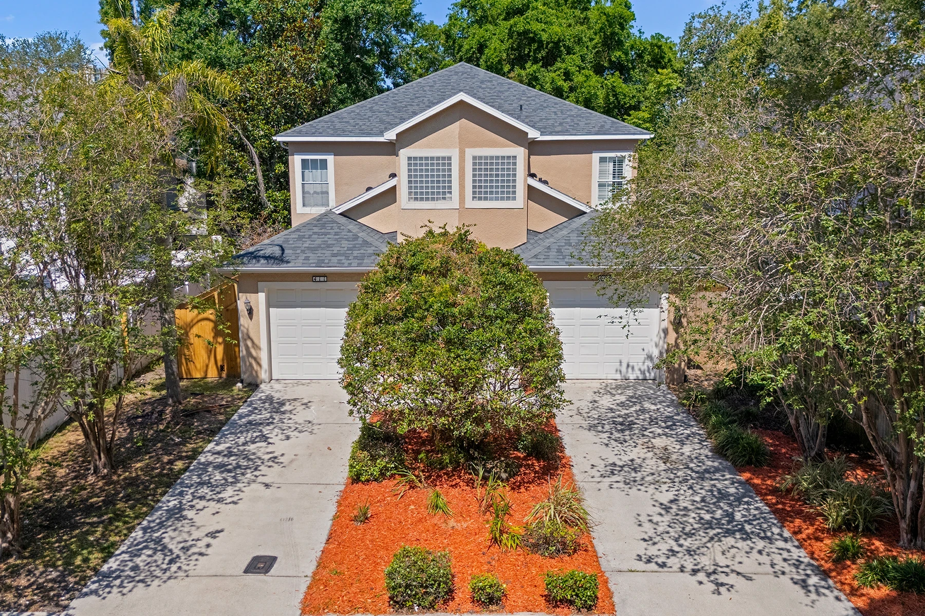 Front exterior of a two-story South Tampa townhome with dual garages, landscaped front yard and mature trees