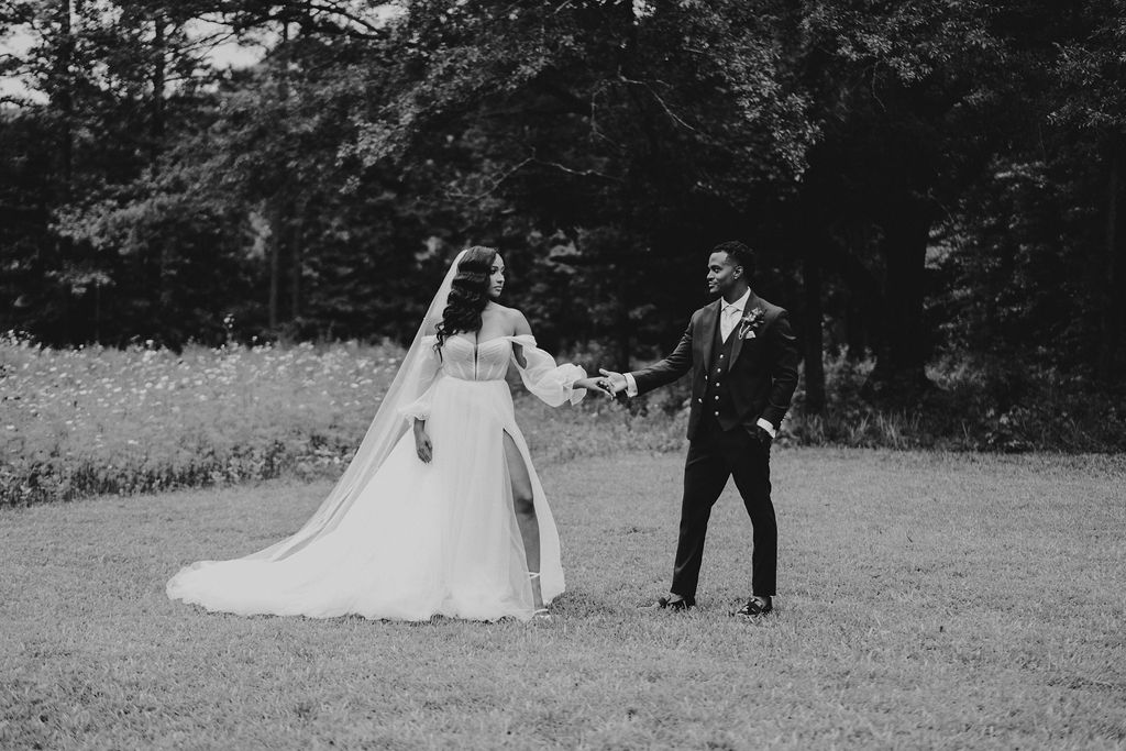 Black-and-white portrait of the newlyweds walking through the meadow.