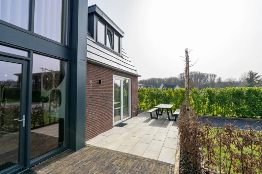 Het terras langs de vakantiewoning met grote ramen en een picknicktafel.