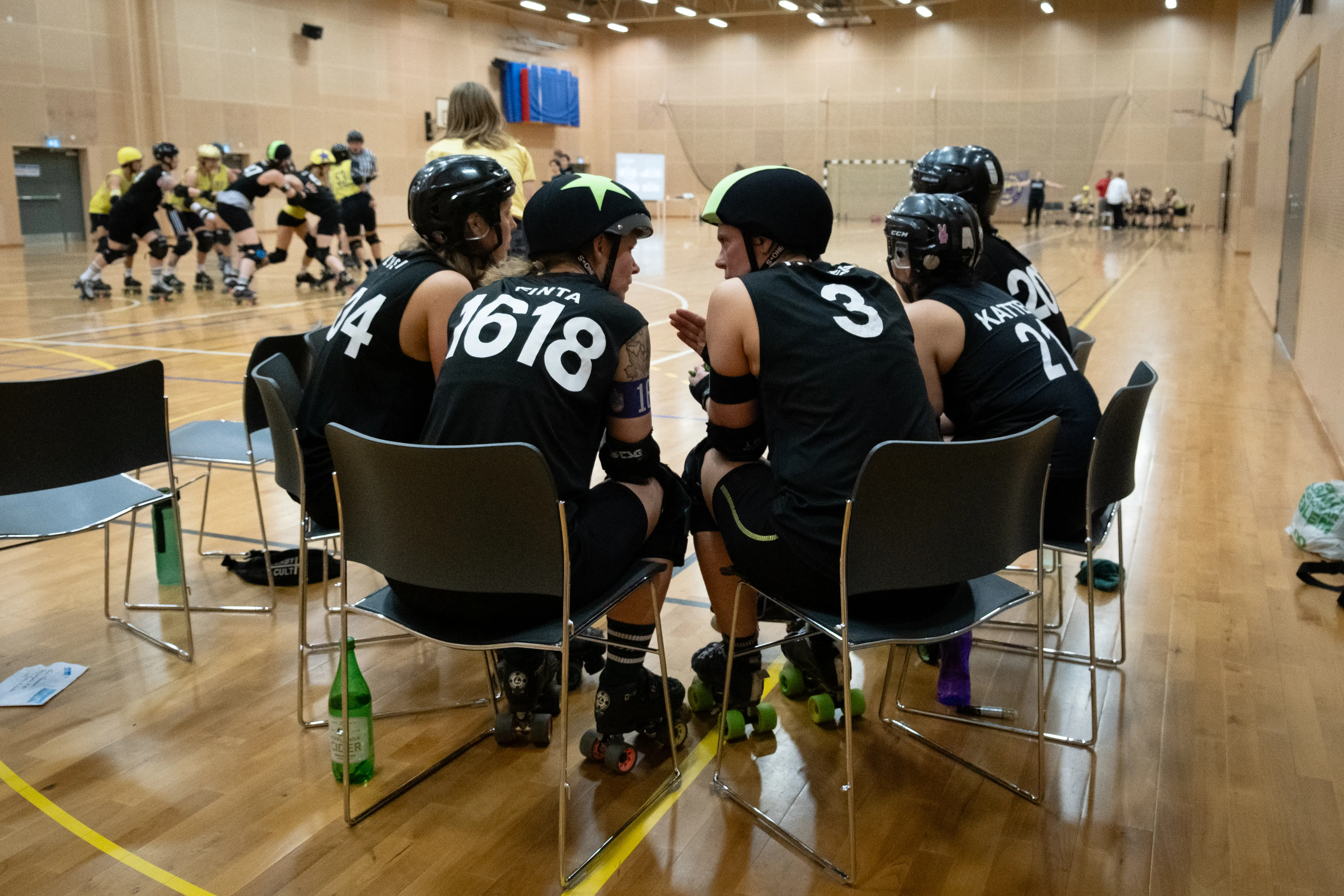 A group of roller derby players sitting on chairs discussing something.