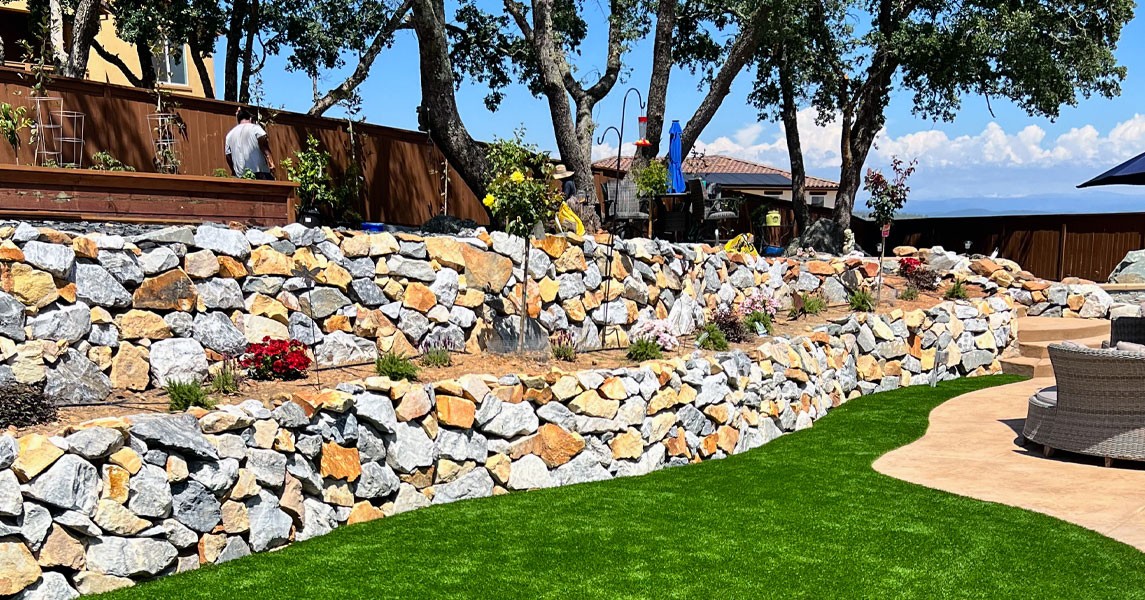 Tiered natural stone retaining walls in El Dorado Hills with planted beds and an artificial turf lawn.
