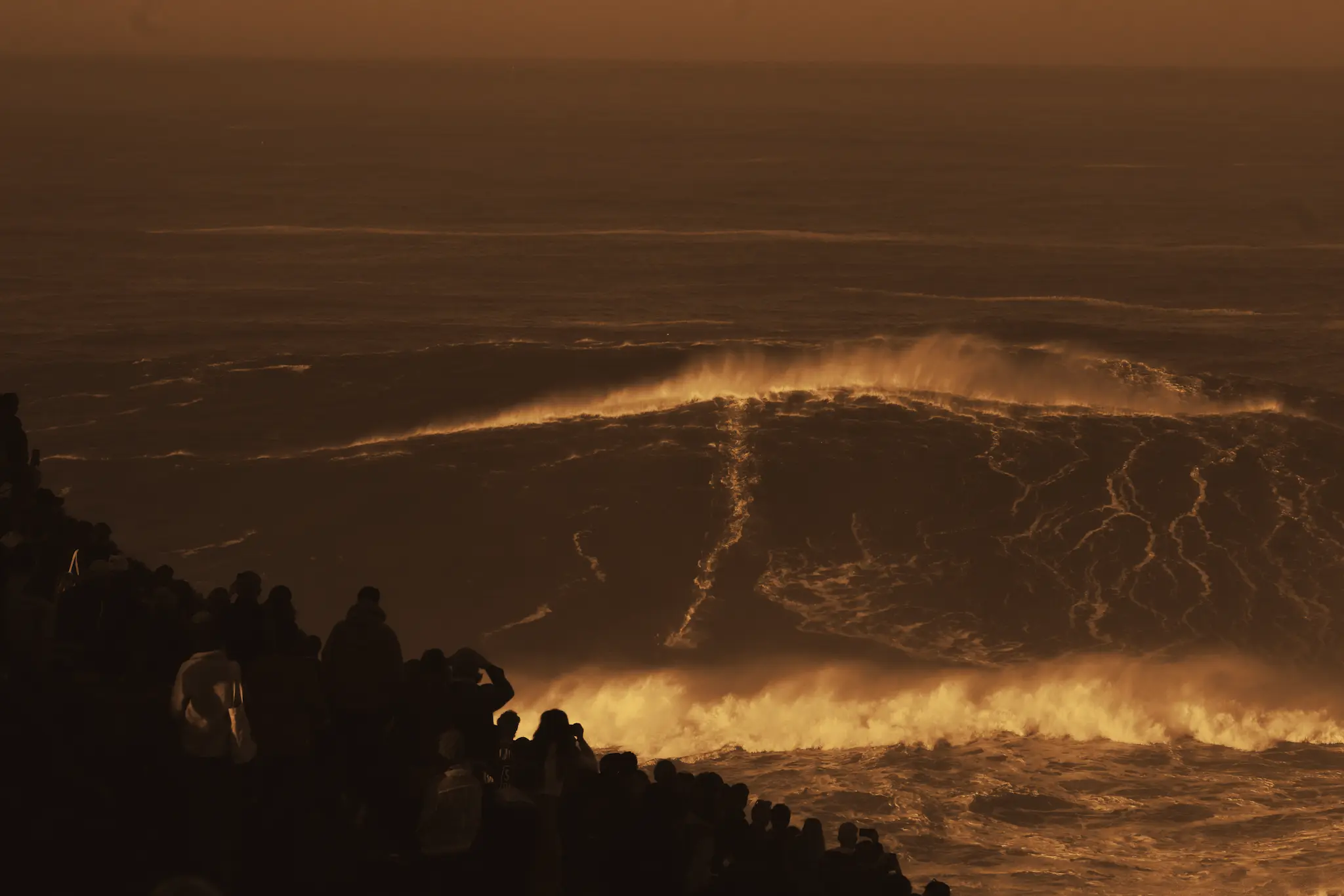 Crowd watching a large wave break at sunset
